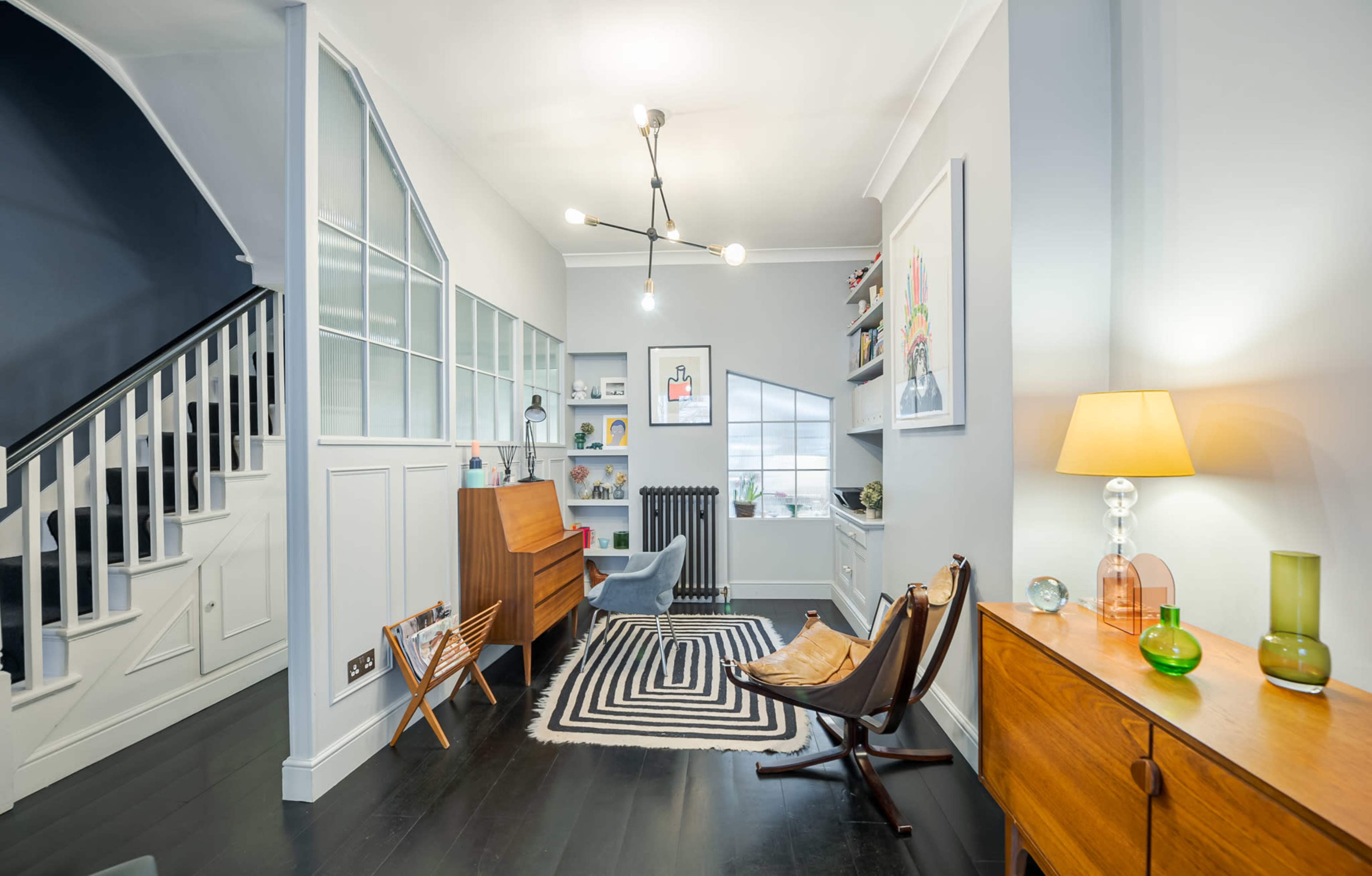A stylish interior features a living area with a piano, a seating arrangement, and a staircase in the background.