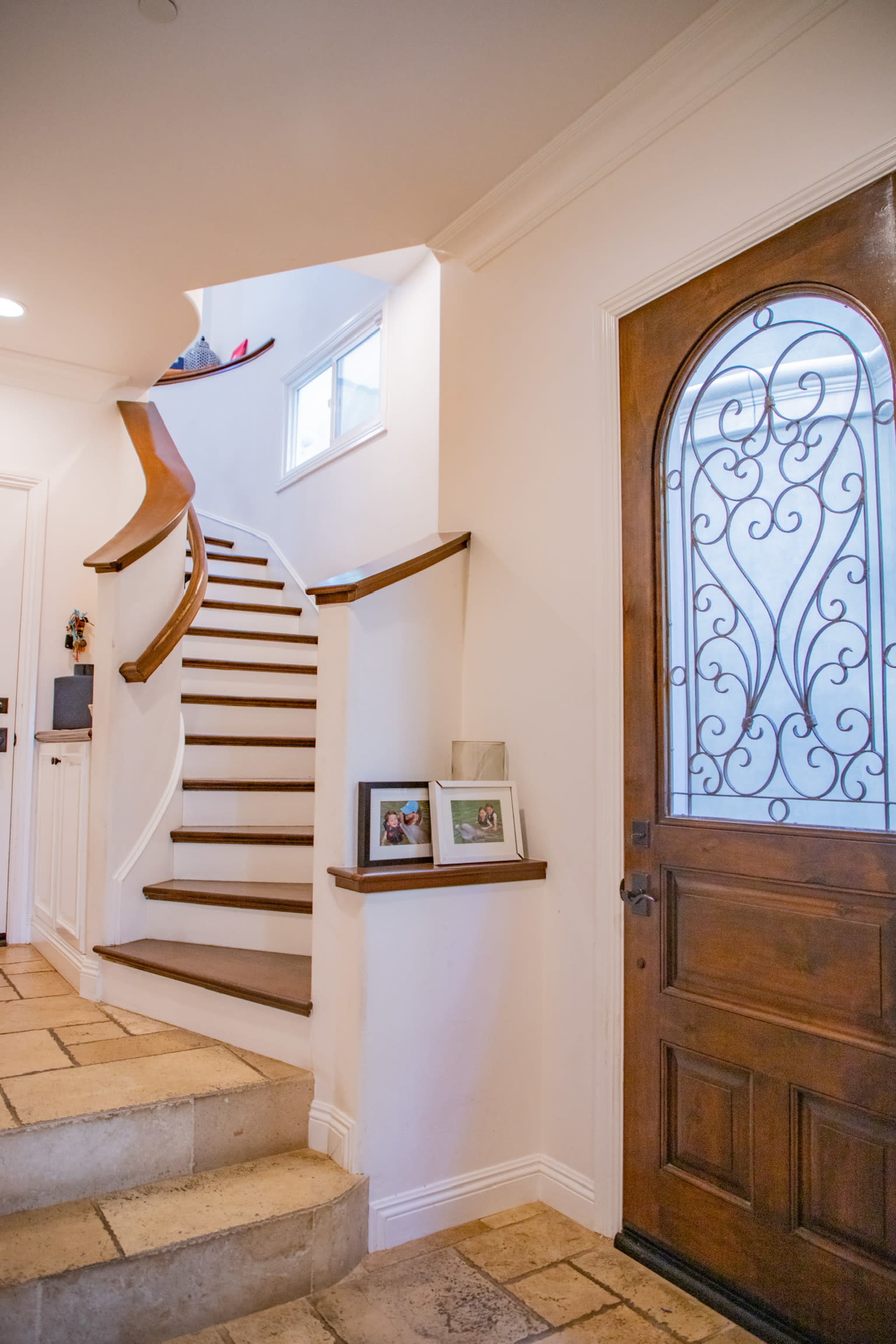 The image shows a foyer with a wooden front door, decorative wrought iron details, and a staircase leading to an upper level.