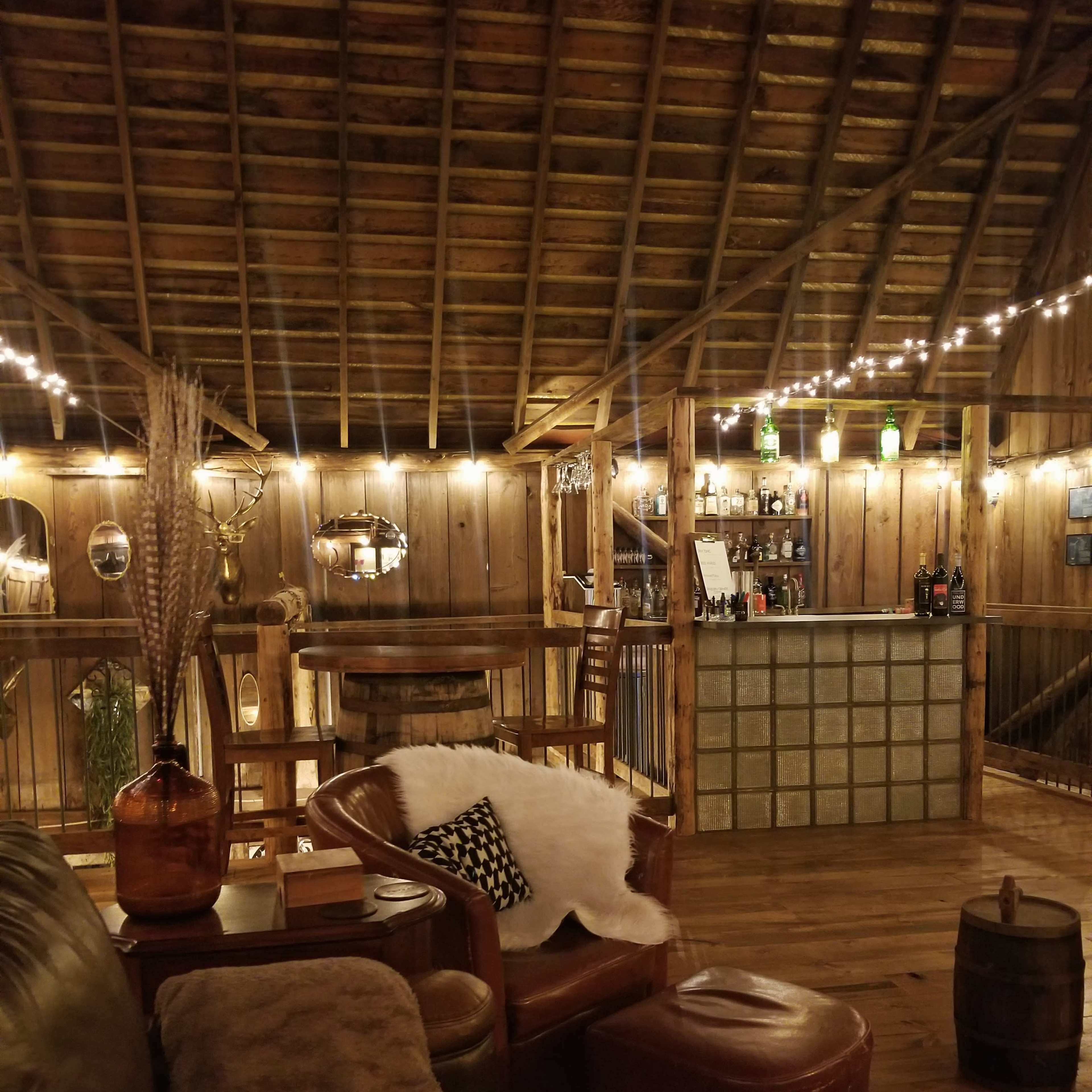 A rustic bar interior with wooden walls, a low ceiling, and string lights illuminating the space.