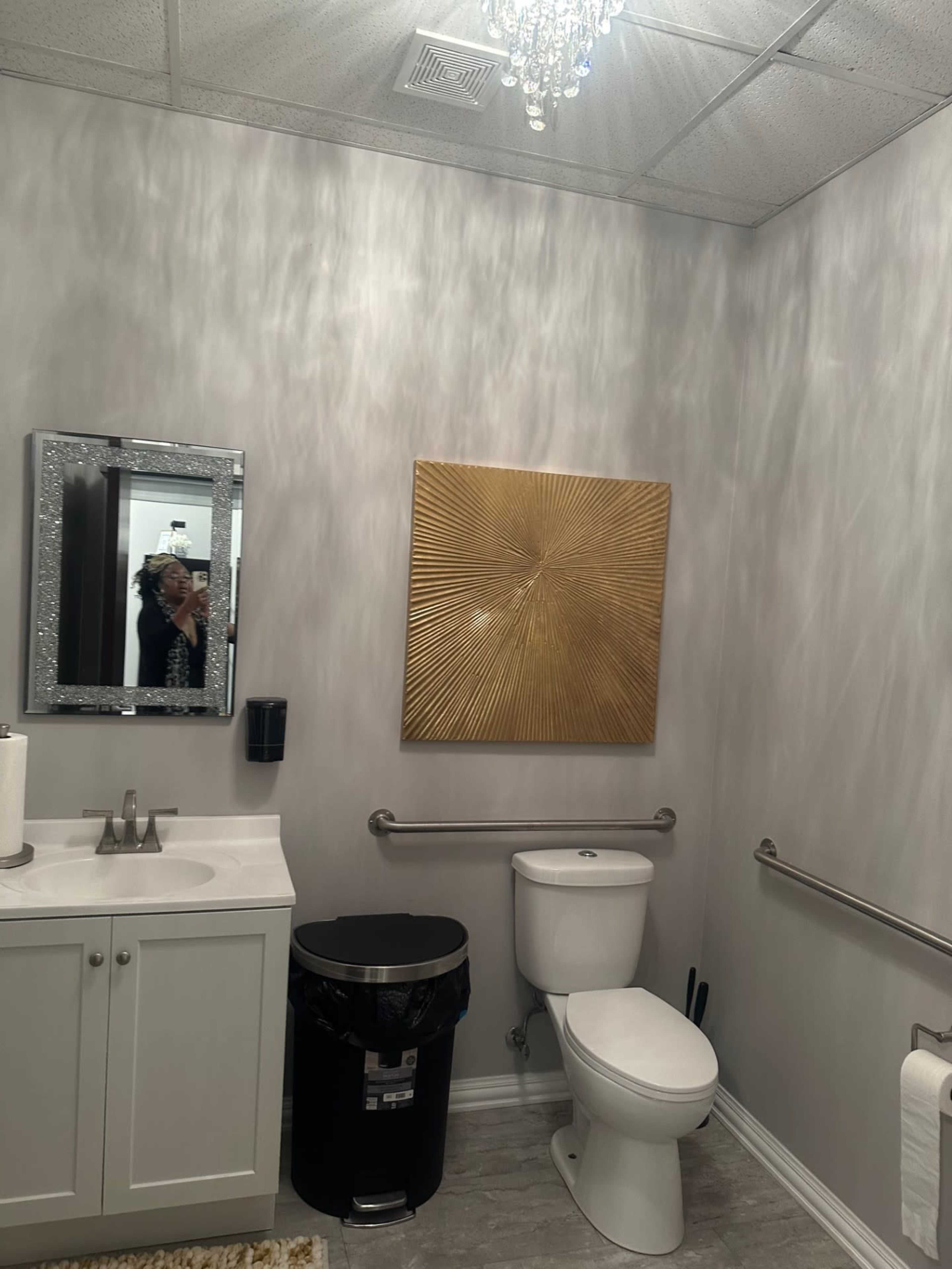 A modern bathroom with a white vanity, a black trash bin, a toilet, and a decorative gold wall art piece.