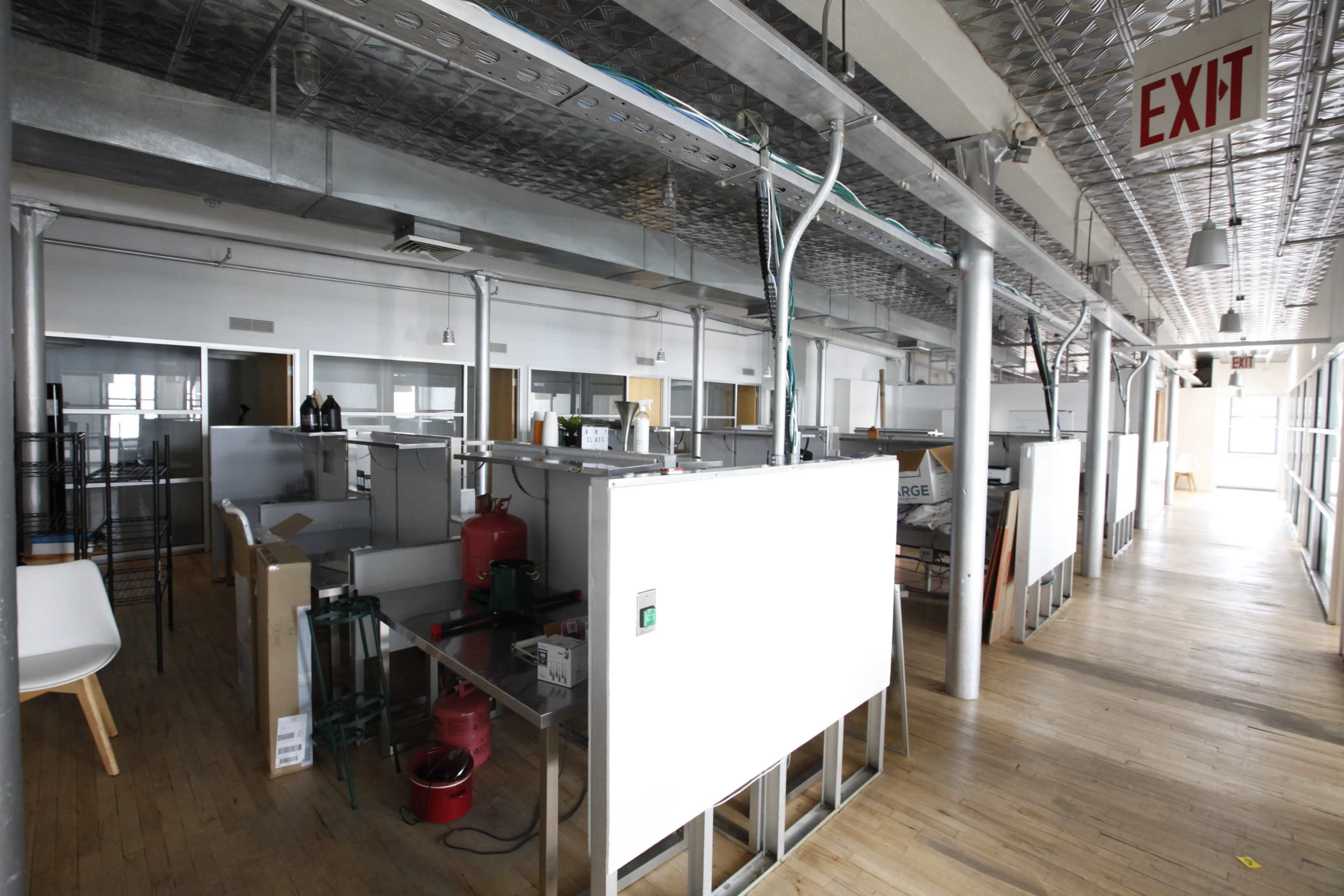 An empty office space features unfinished workstations, wood flooring, and visible exit signage.