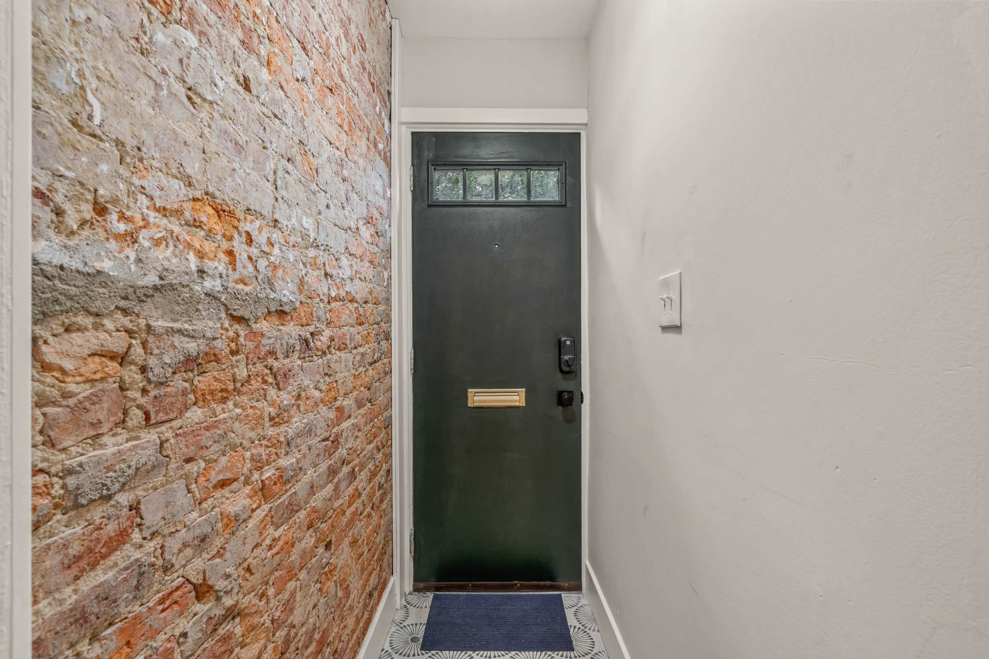 A narrow hallway with a brick wall on one side and a dark green front door at the end.