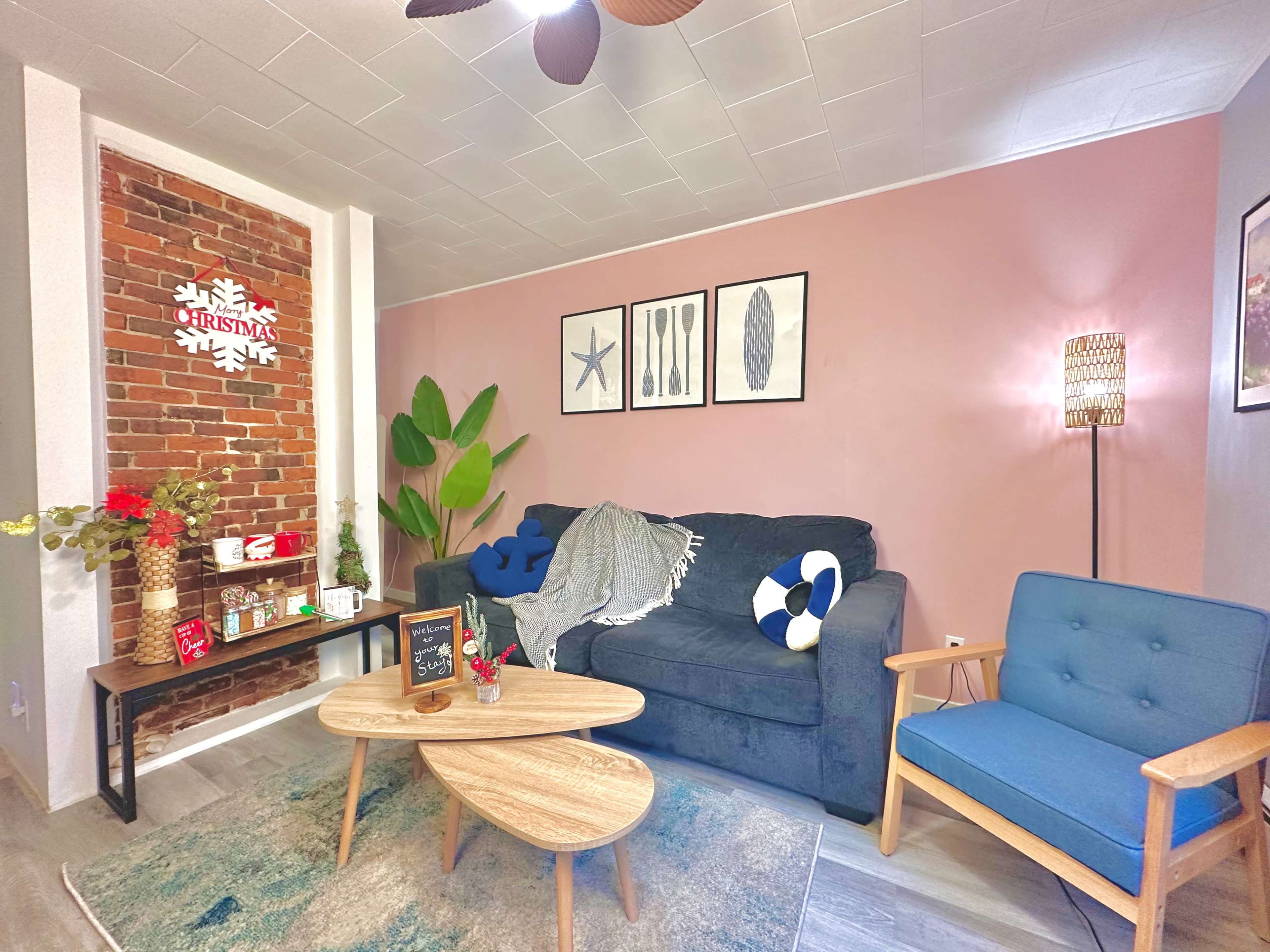 The living room features a blue couch with a throw blanket, a wooden coffee table, and a decorative wall with brick, plants, and framed artwork.