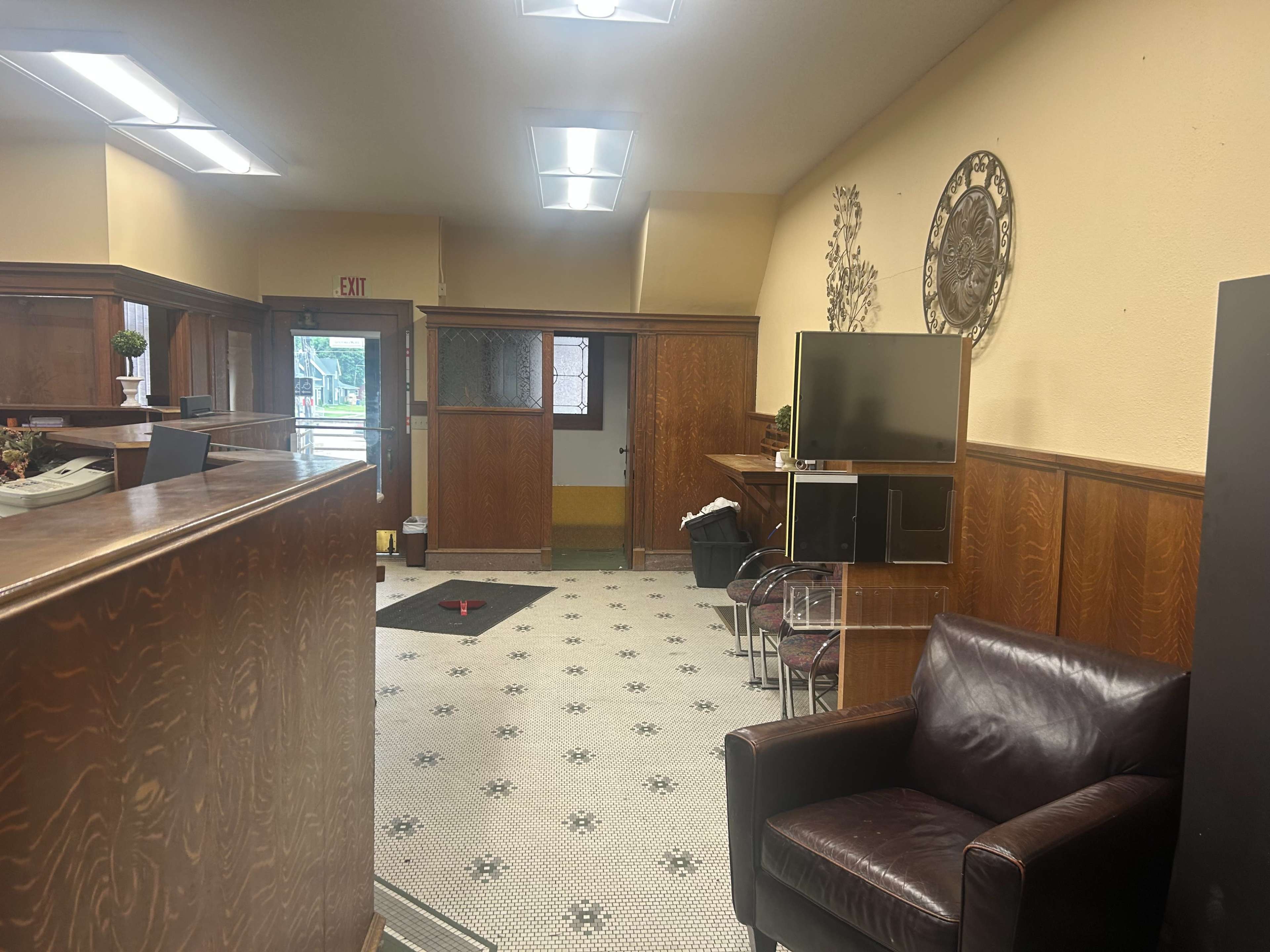The image shows a wooden-paneled reception area with a brown leather chair, a television on a stand, and a small carpeted section on the floor.
