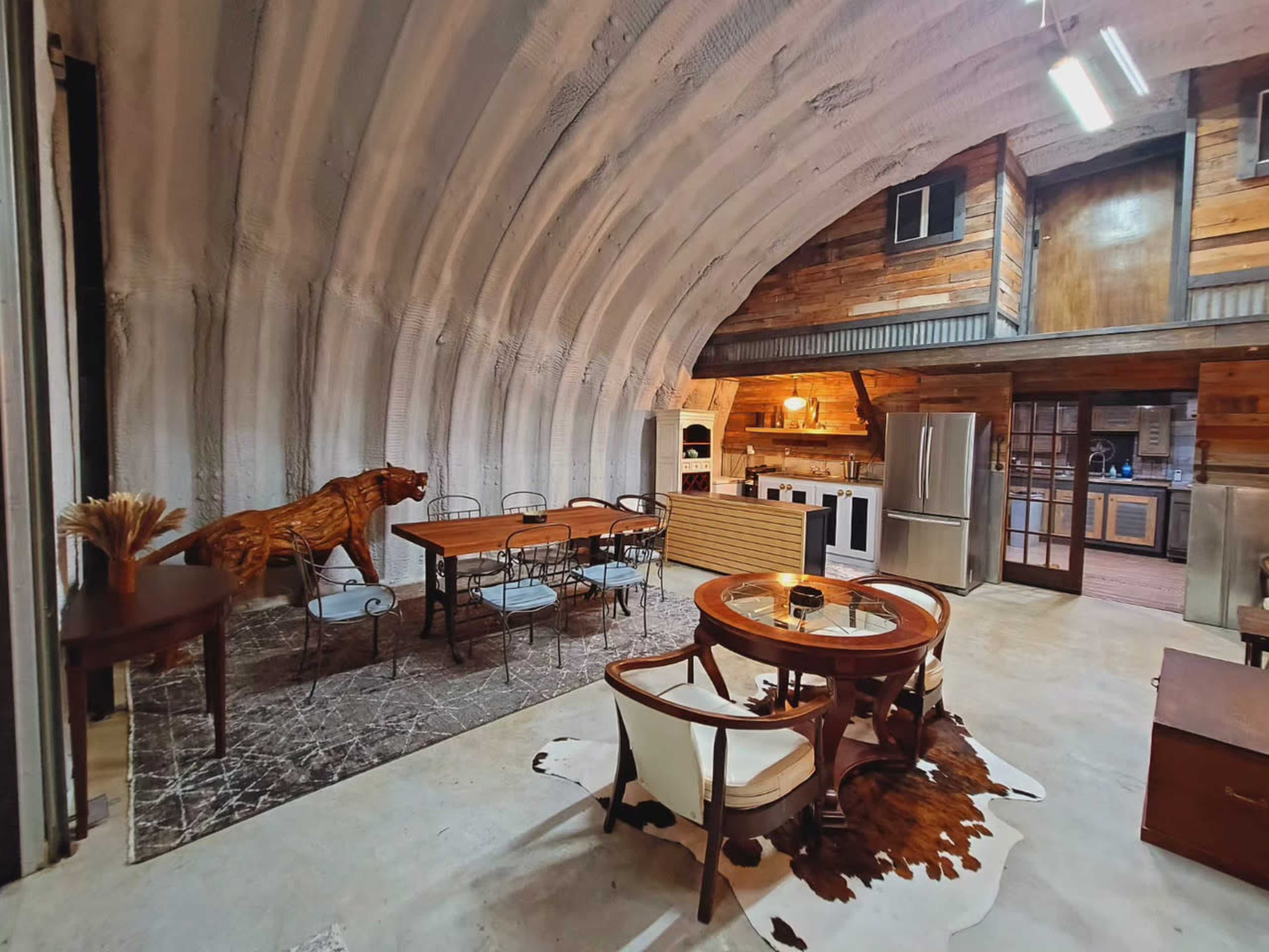 The spacious kitchen and dining area feature a curved, textured ceiling, wooden accents, and a mix of rustic and modern furnishings.