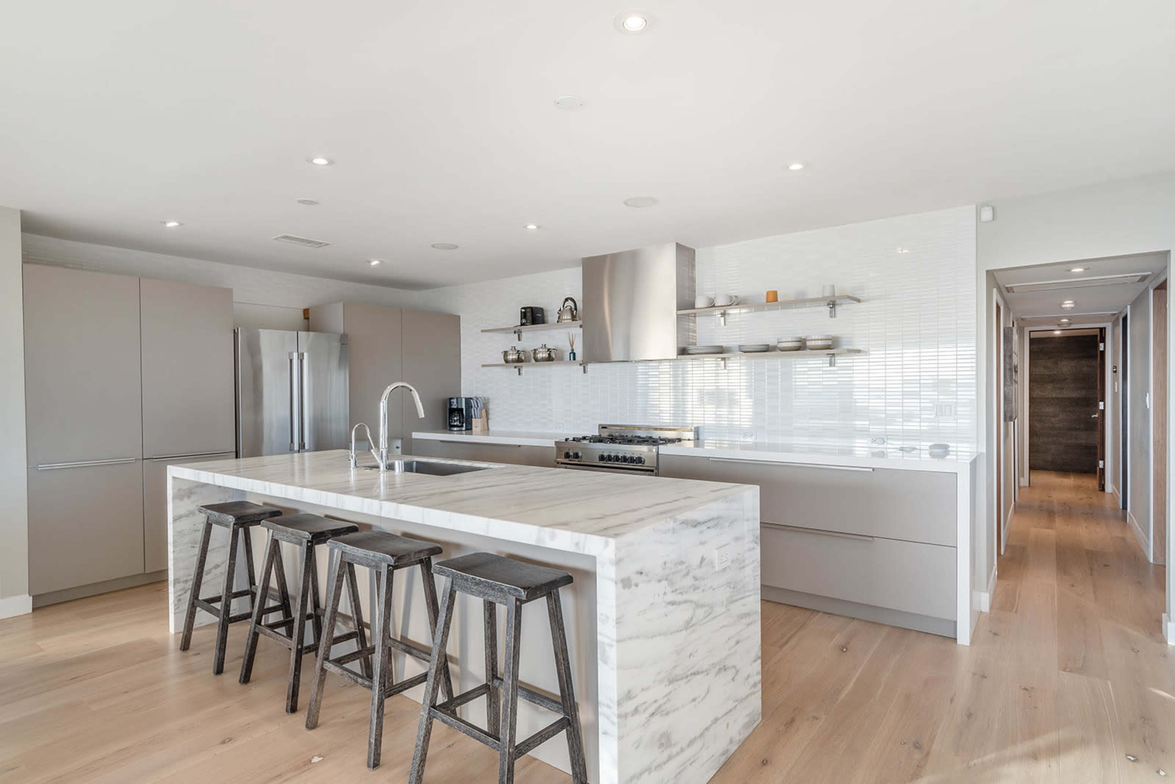 The image shows a modern kitchen with a large marble island, stainless steel appliances, and a minimalist design.