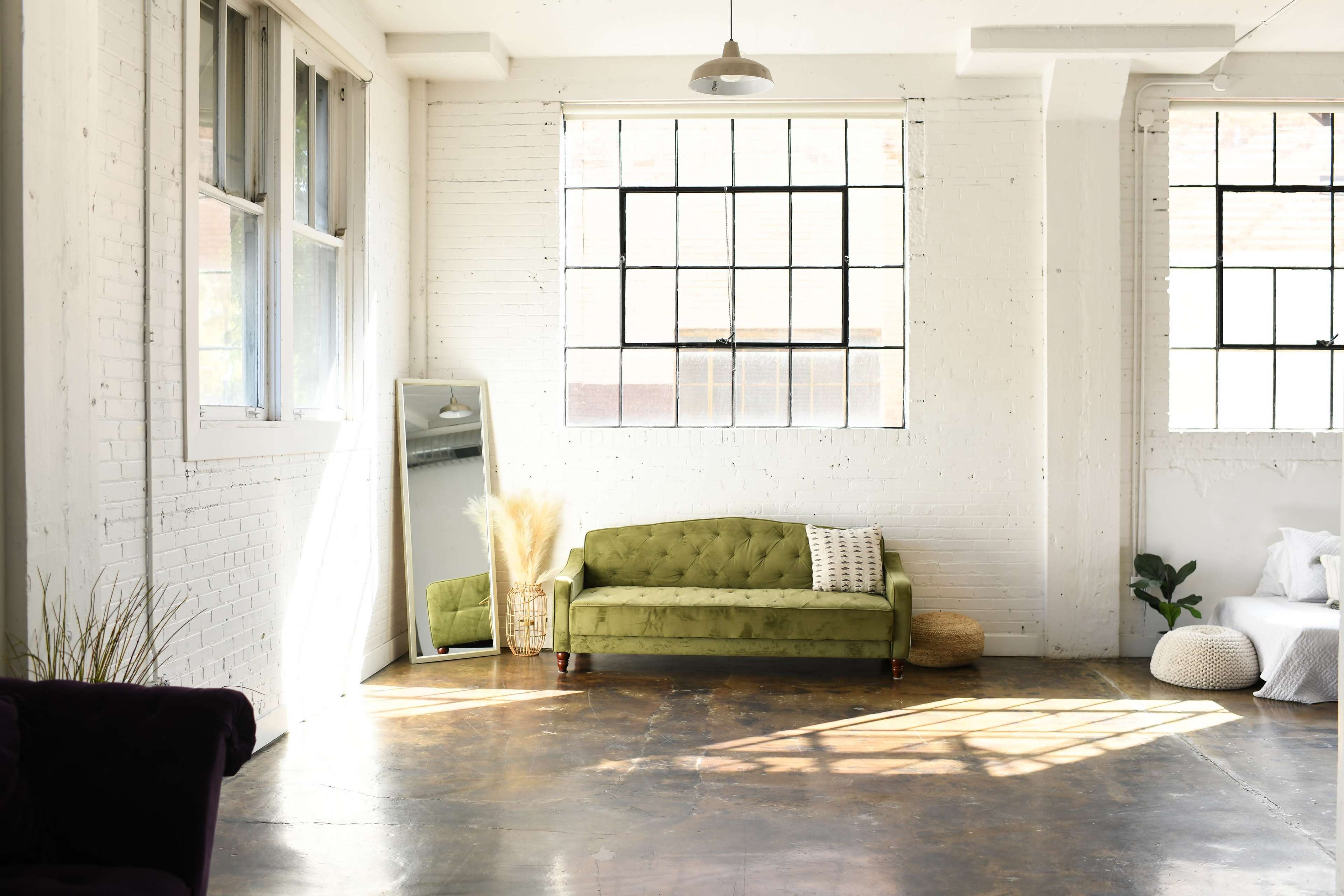 A bright, spacious room featuring a green sofa, large windows, and minimal decor.