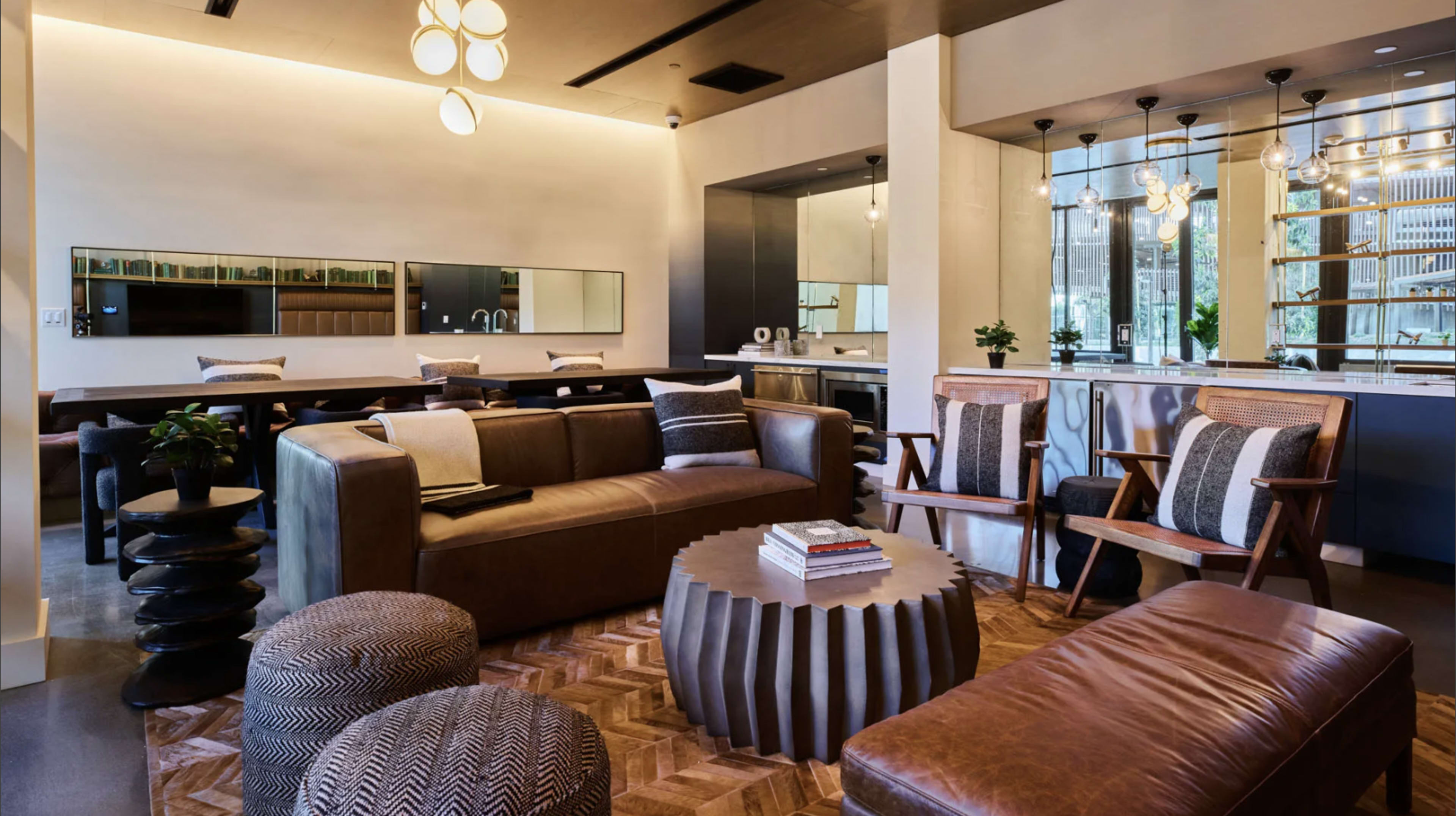 The image shows a modern living space with a mix of leather sofas, wooden chairs, and a circular coffee table, surrounded by large windows and decorative lighting.