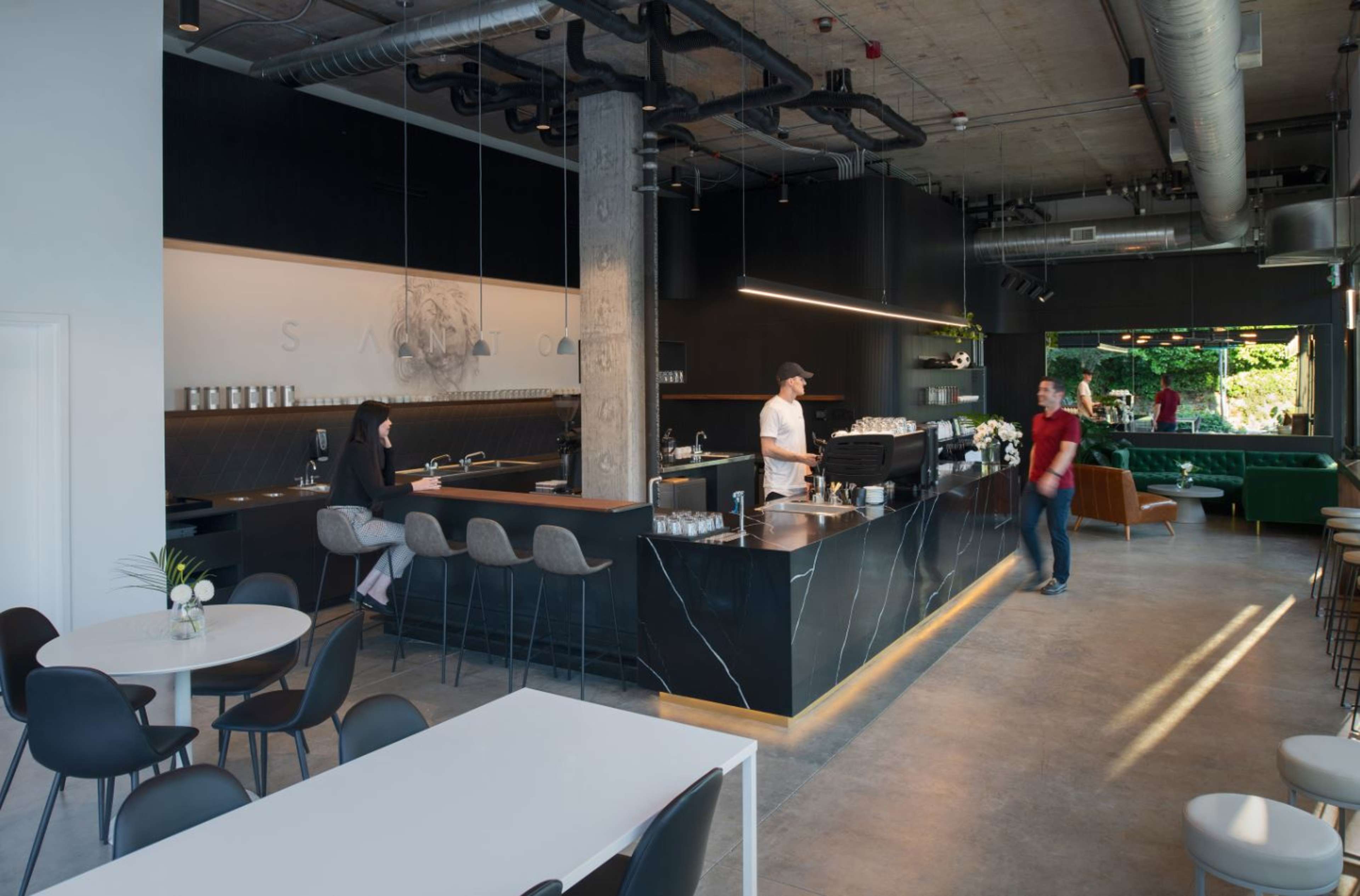 A modern coffee shop features a sleek counter with baristas serving customers, surrounded by minimalist furniture and large windows allowing natural light.