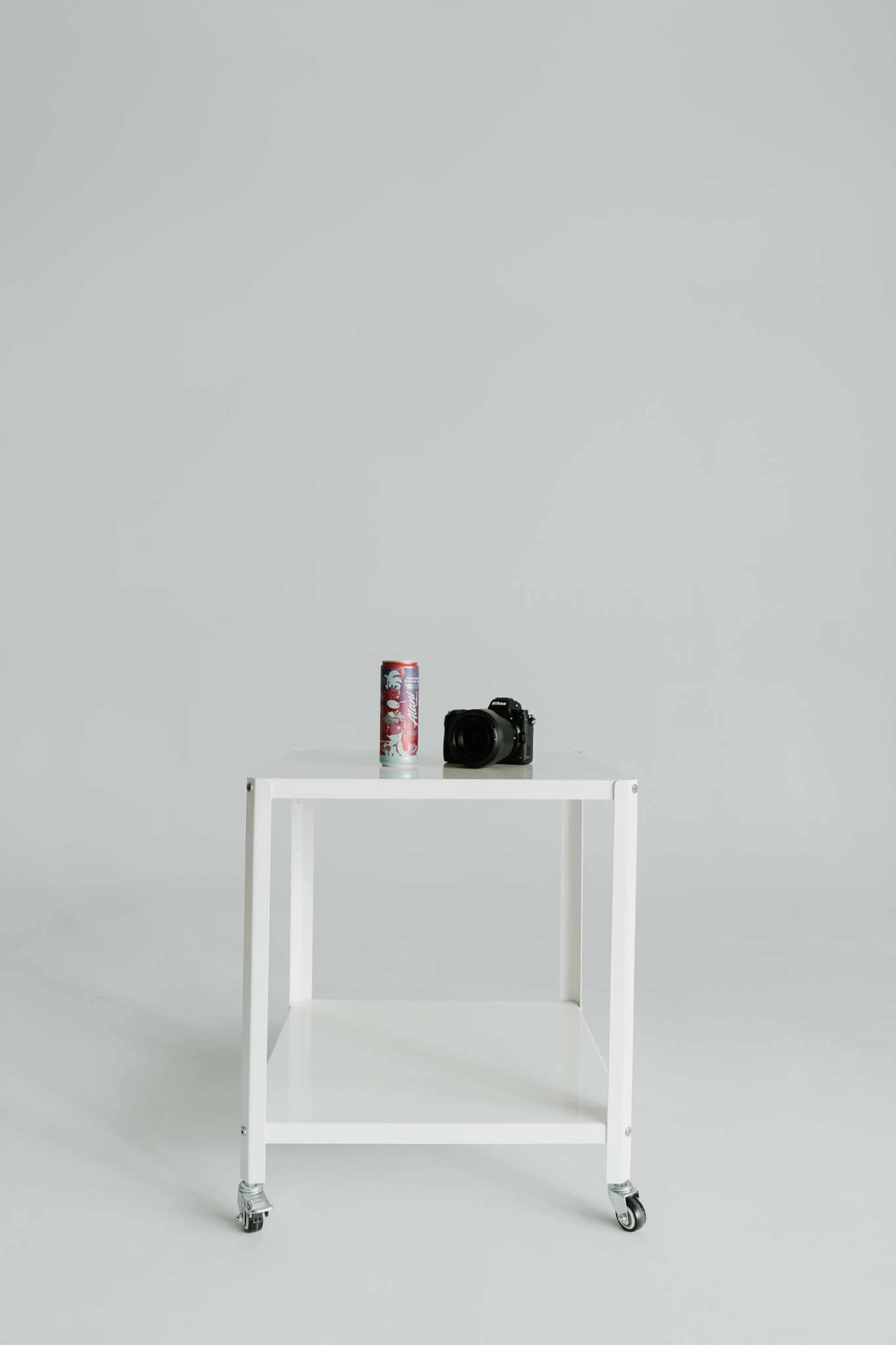A white table on wheels holds a can and a camera against a gray background.