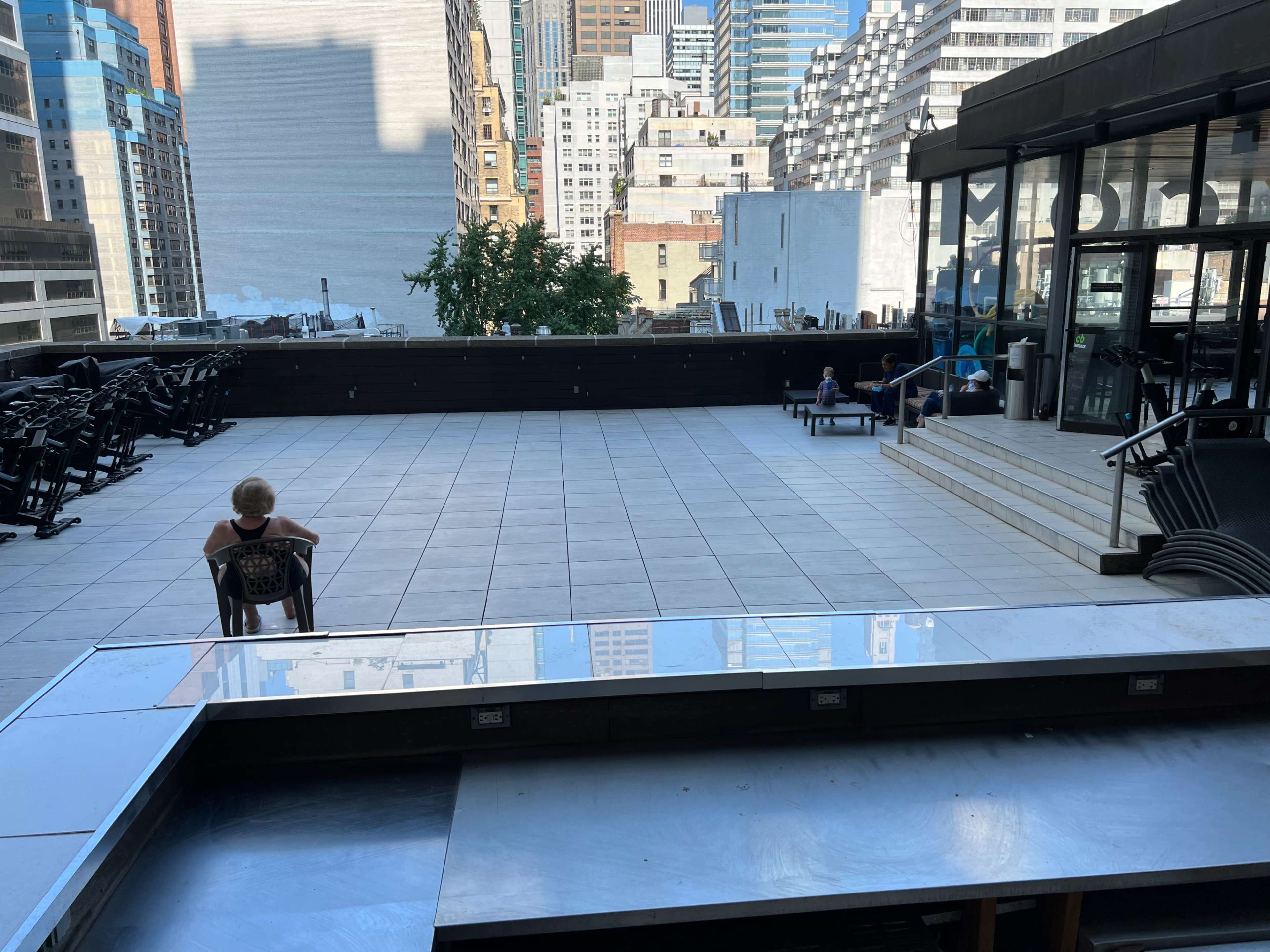 A spacious outdoor terrace is shown, featuring a patio with several empty chairs and tables, overlooking city buildings.