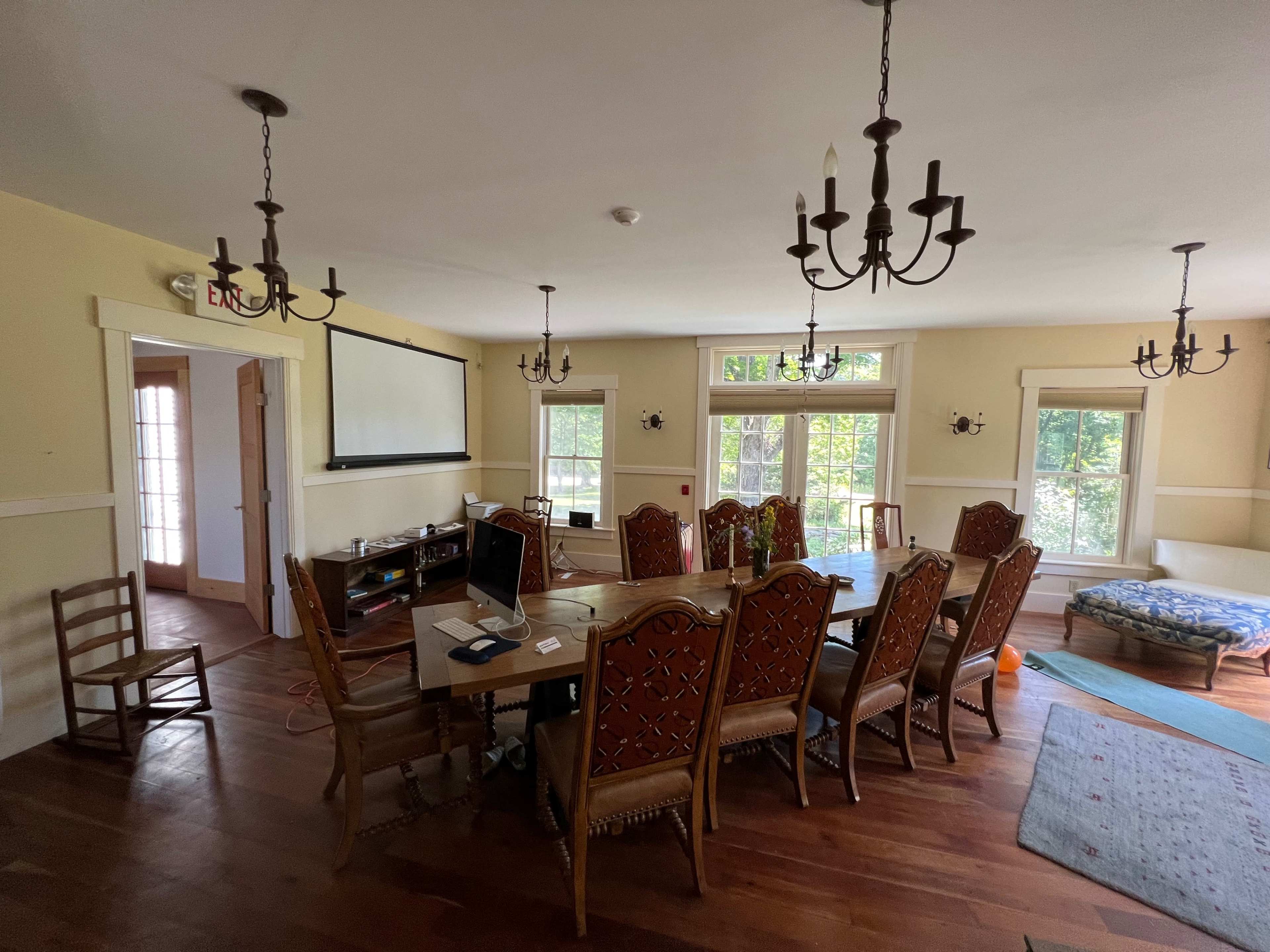 A spacious dining room features a long wooden table surrounded by ornate chairs, with large windows allowing natural light to fill the space.