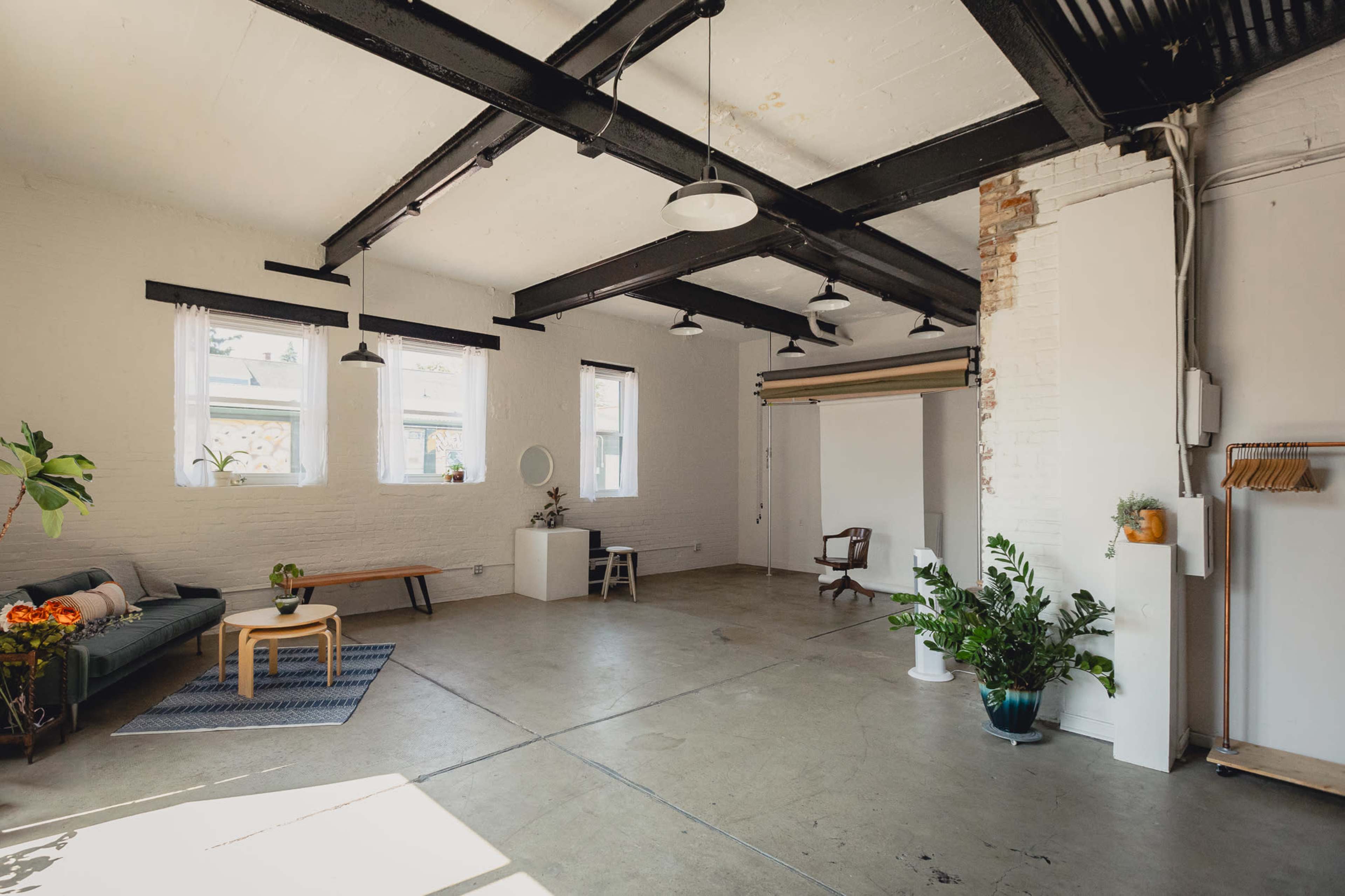 A spacious, modern interior with a green sofa, wooden bench, and plants, under exposed beams and natural light from large windows.