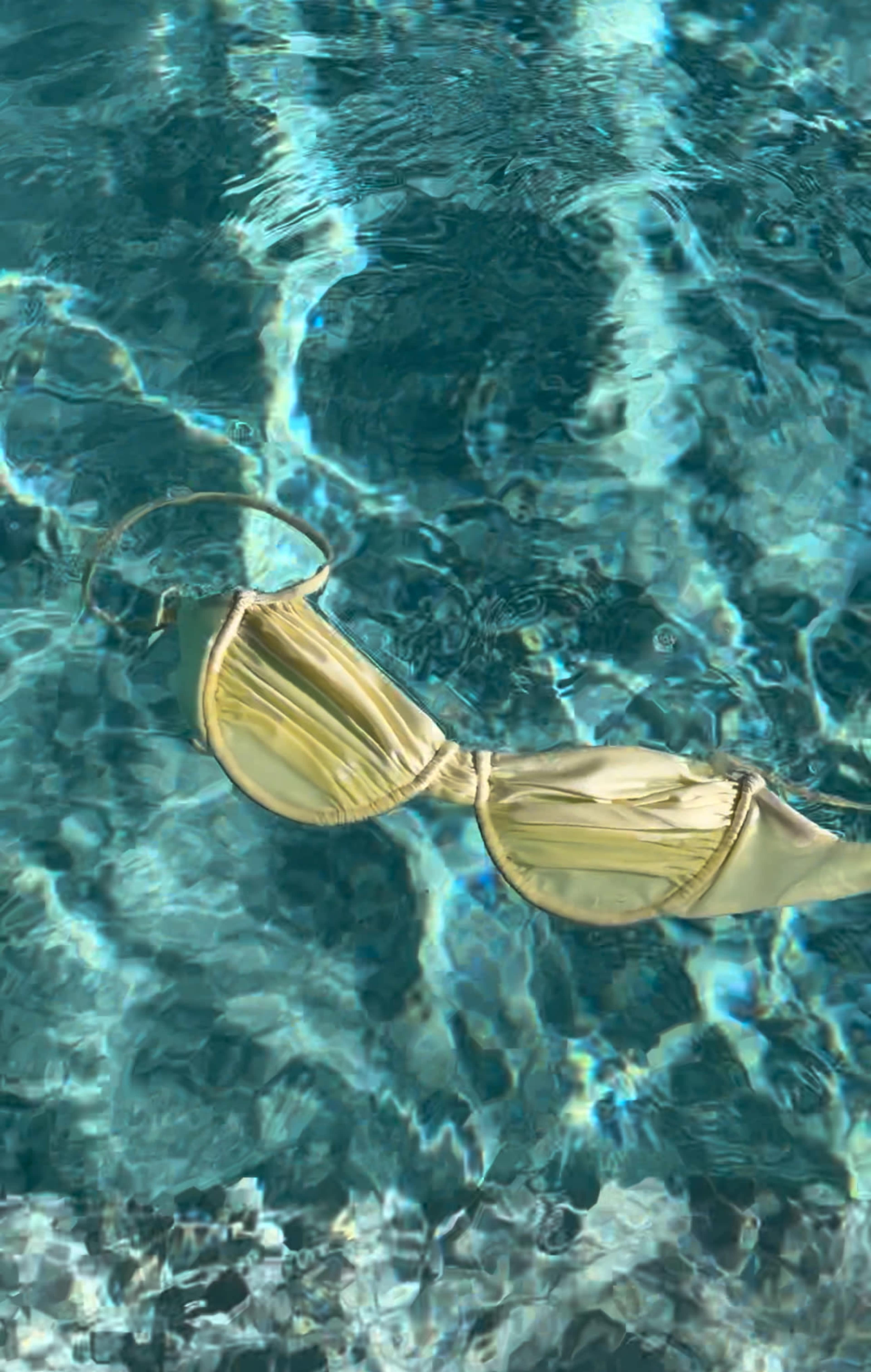 A yellow bikini top floats on the surface of a clear swimming pool.