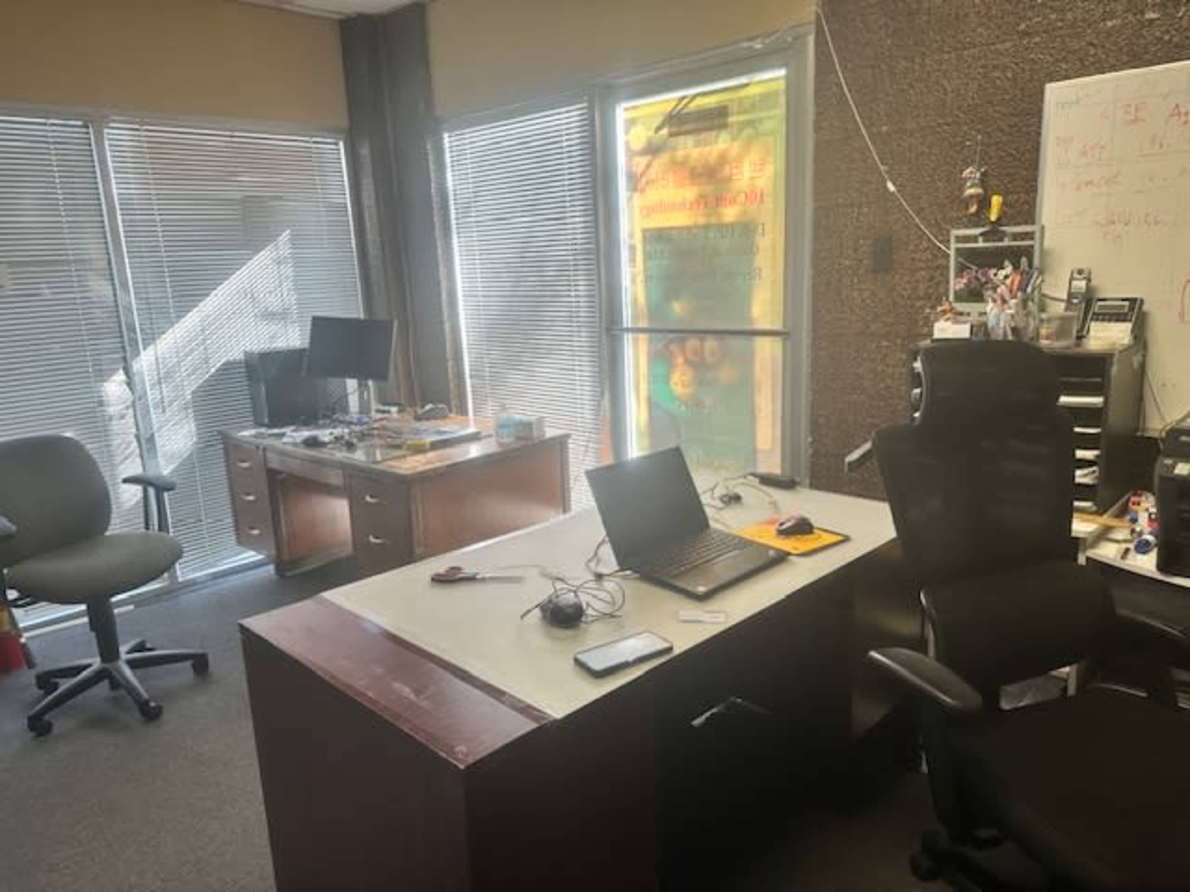The image shows an office space with two desks, chairs, computers, and a whiteboard, illuminated by natural light from windows.