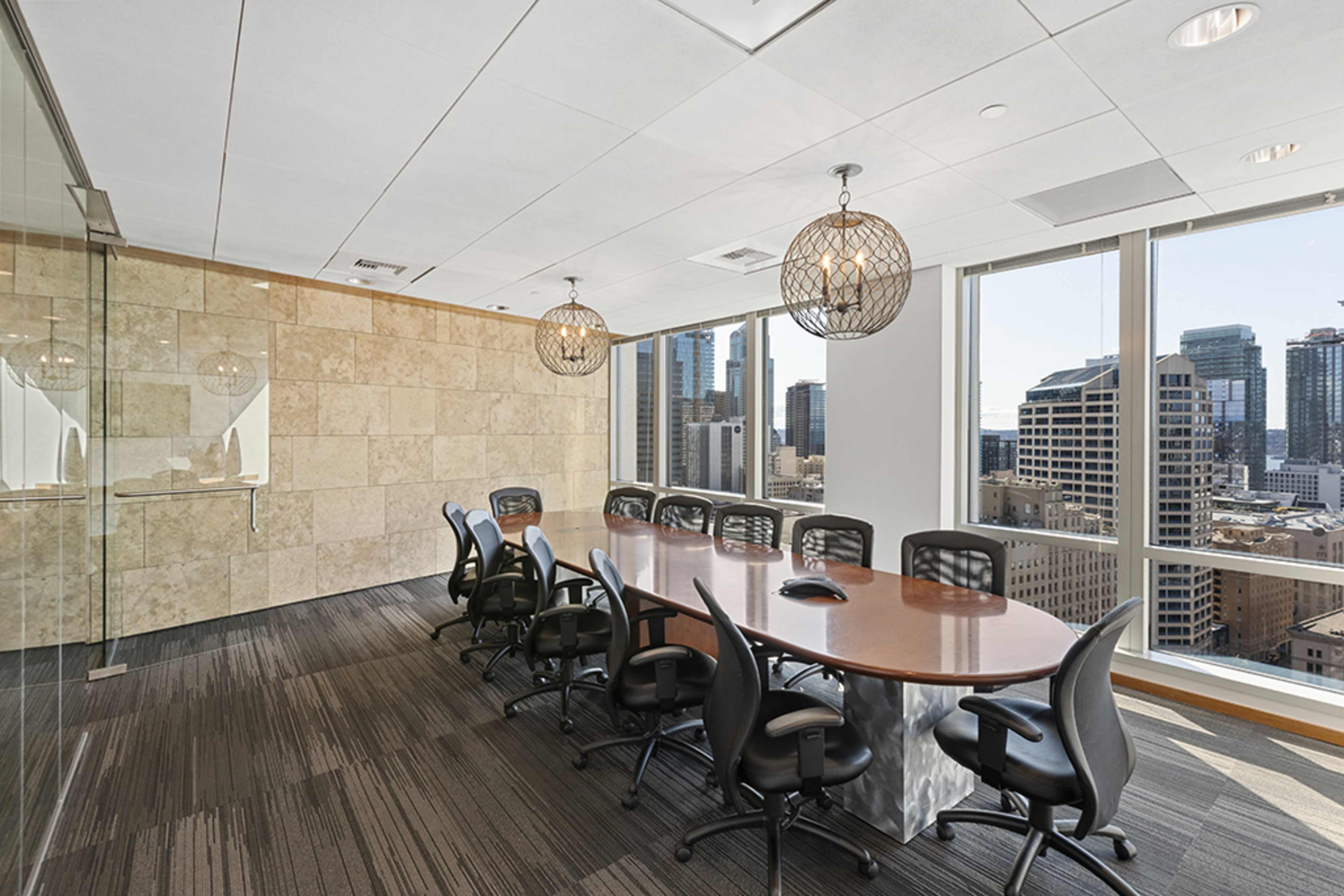 A long conference table with black chairs is positioned in a modern meeting room featuring large windows that offer a view of the city skyline.