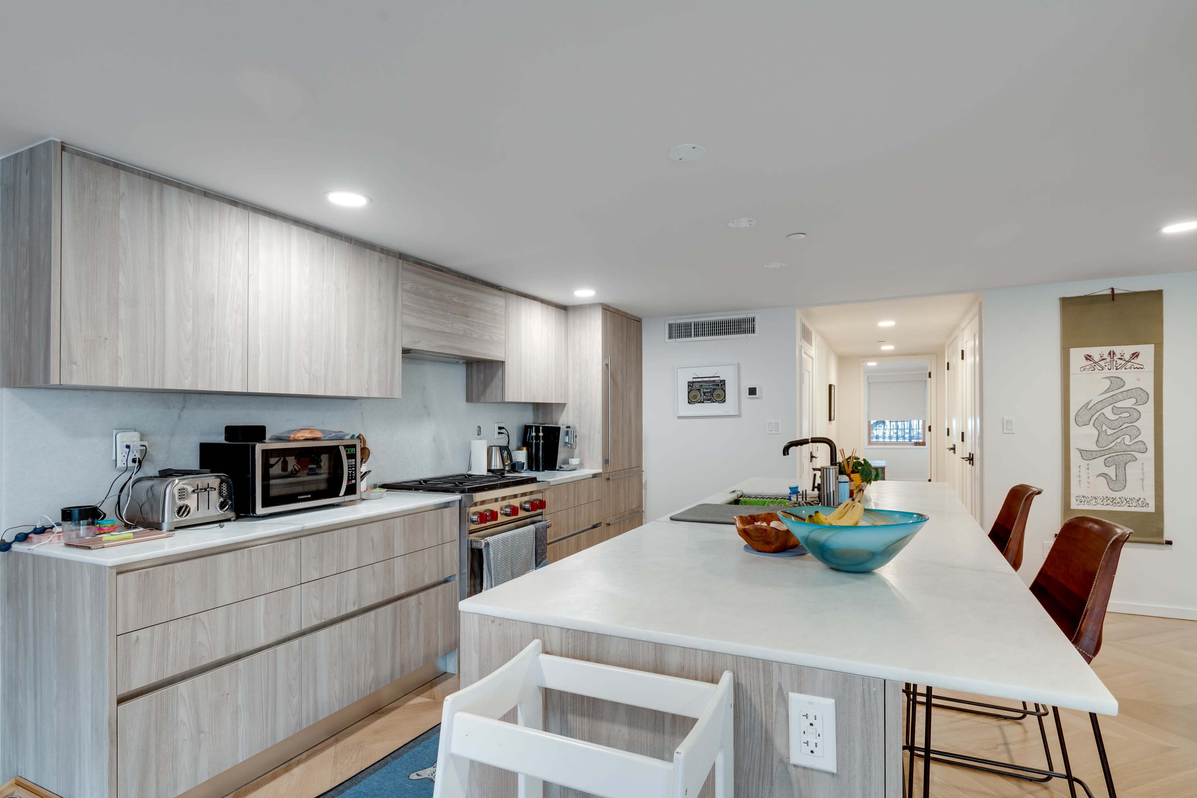A modern kitchen with light wood cabinetry, a gas stove, and an island with a bowl of fruit.
