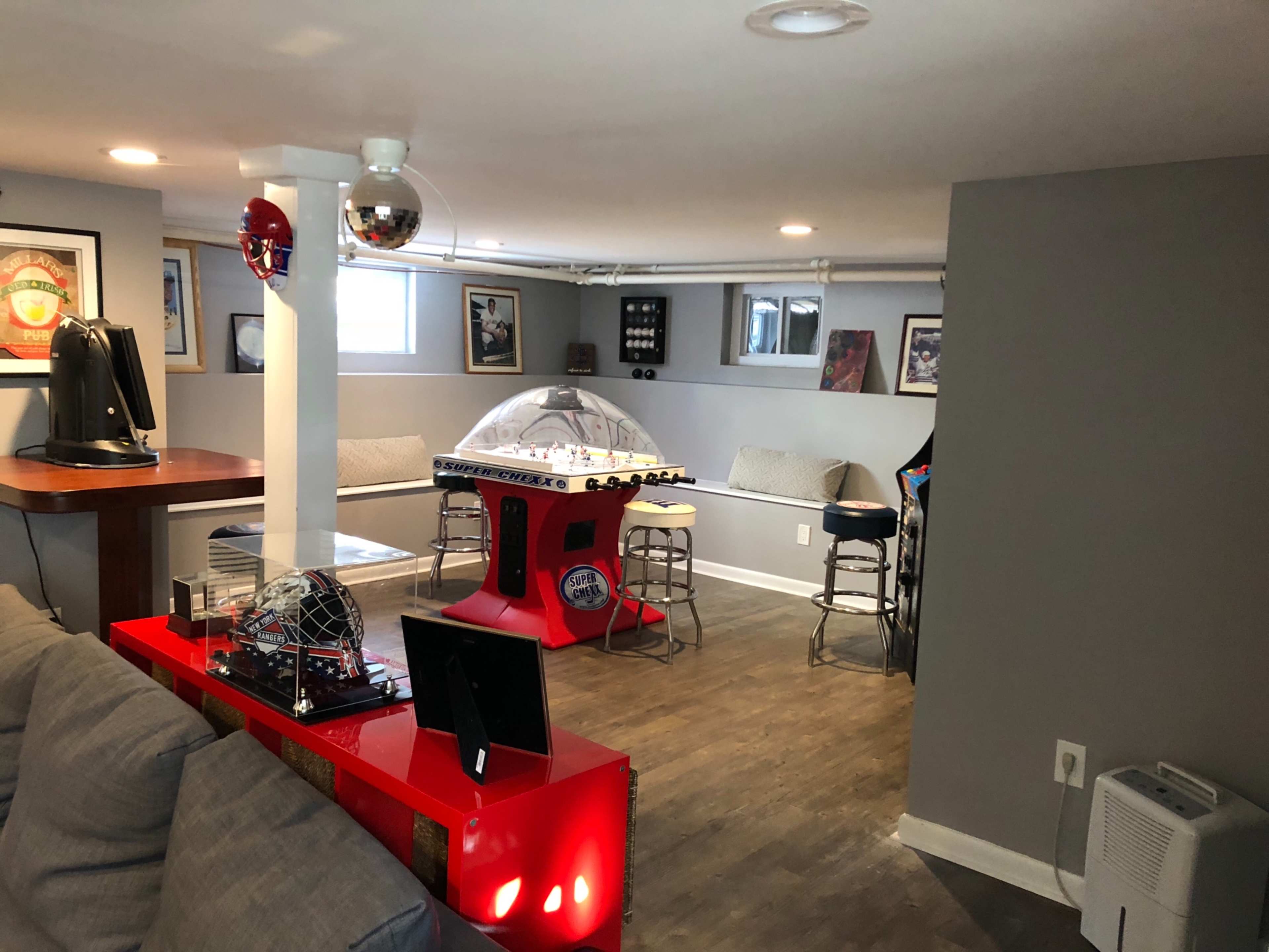 A basement recreation area featuring a foosball table, a bar counter with stools, and a seating area along the walls.