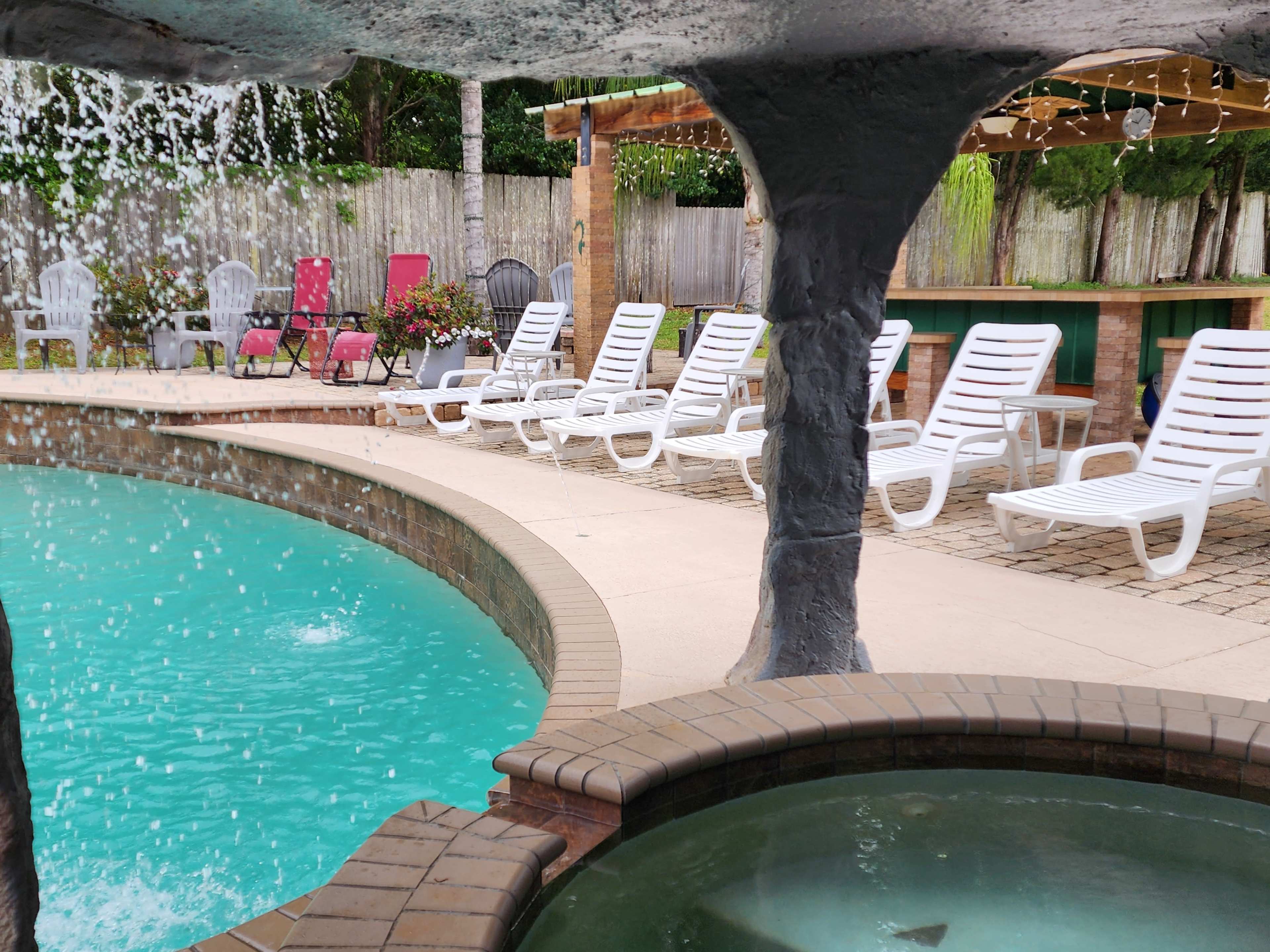 A swimming pool area with lounge chairs arranged around it and a water feature cascading from a stone structure.