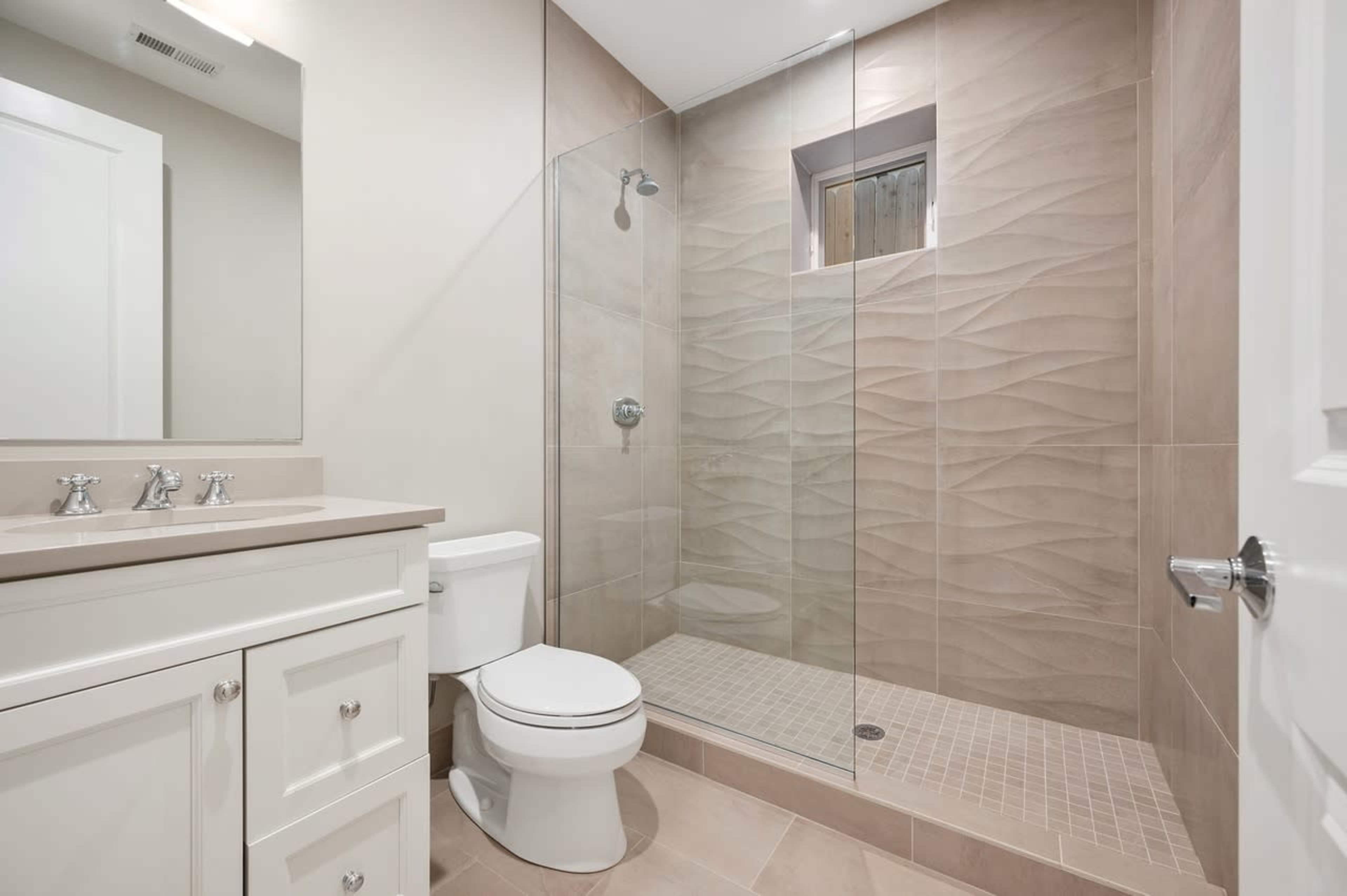 A modern bathroom featuring a glass shower, a toilet, and a sink with a mirror above it.