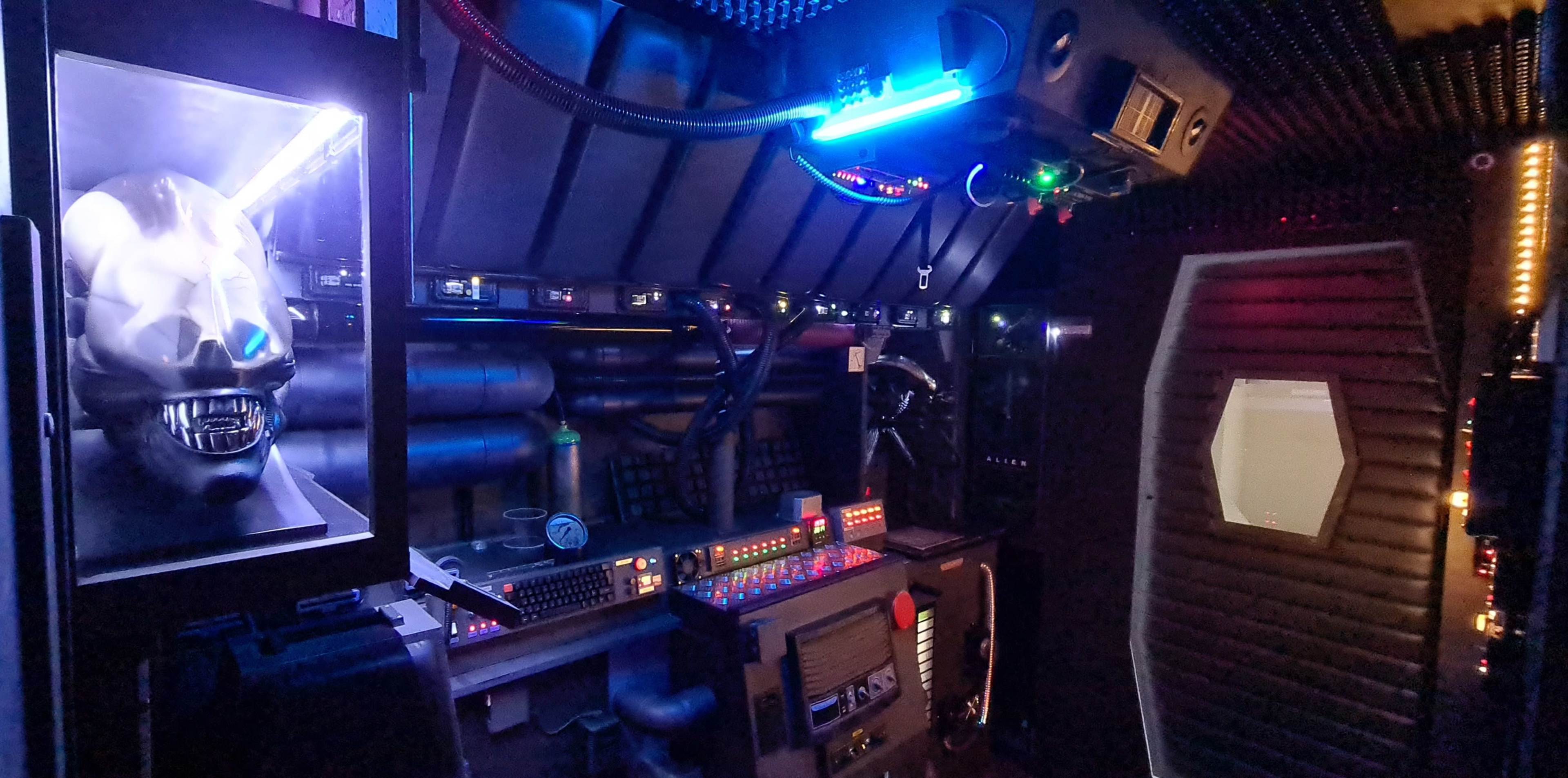 A futuristic control room featuring a sleek black design with various illuminated panels, a robotic head display, and an array of technological equipment.