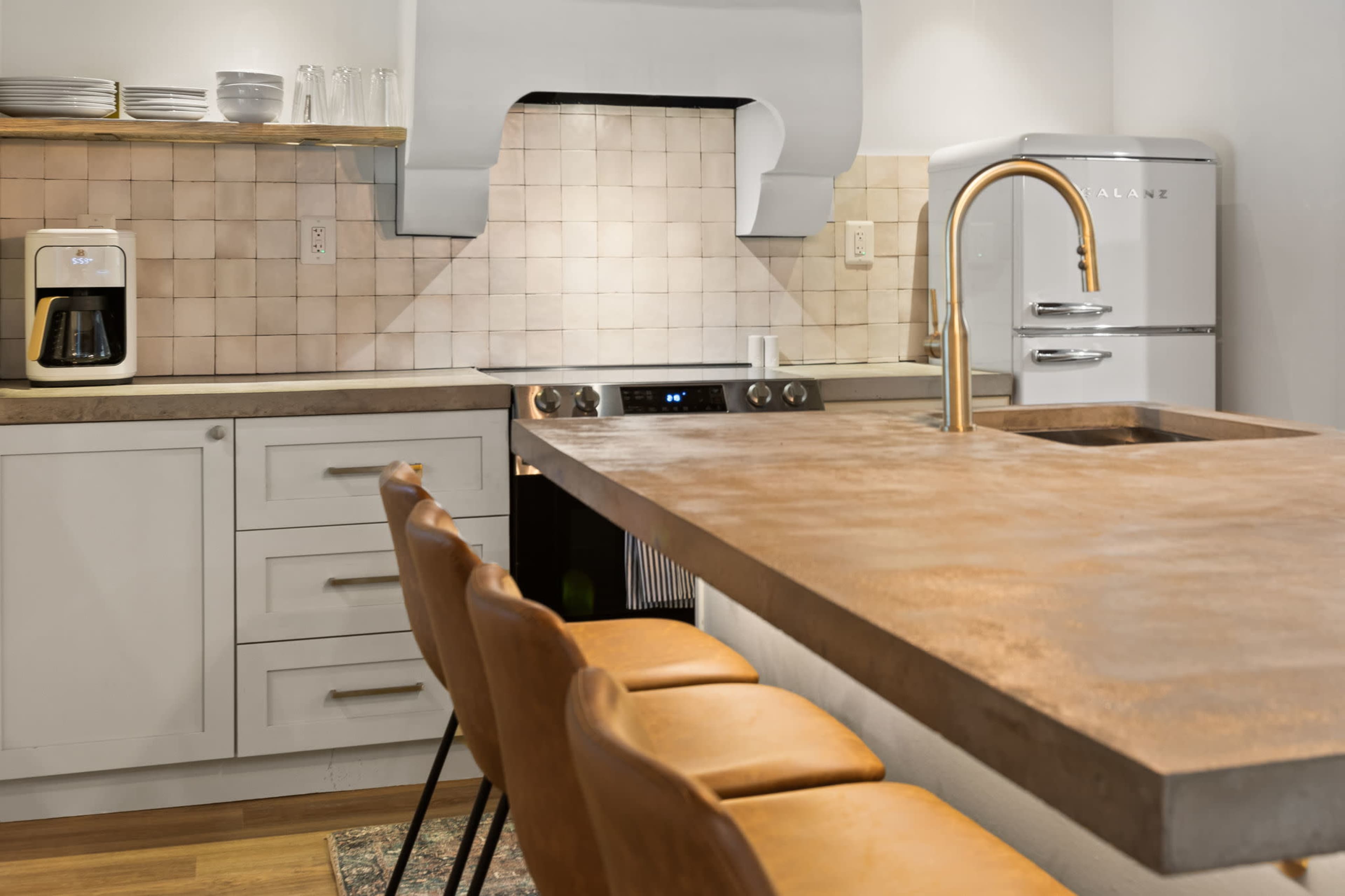 A modern kitchen with a copper countertop, beige tile backsplash, white cabinetry, a stainless steel stove, and a retro-style refrigerator.