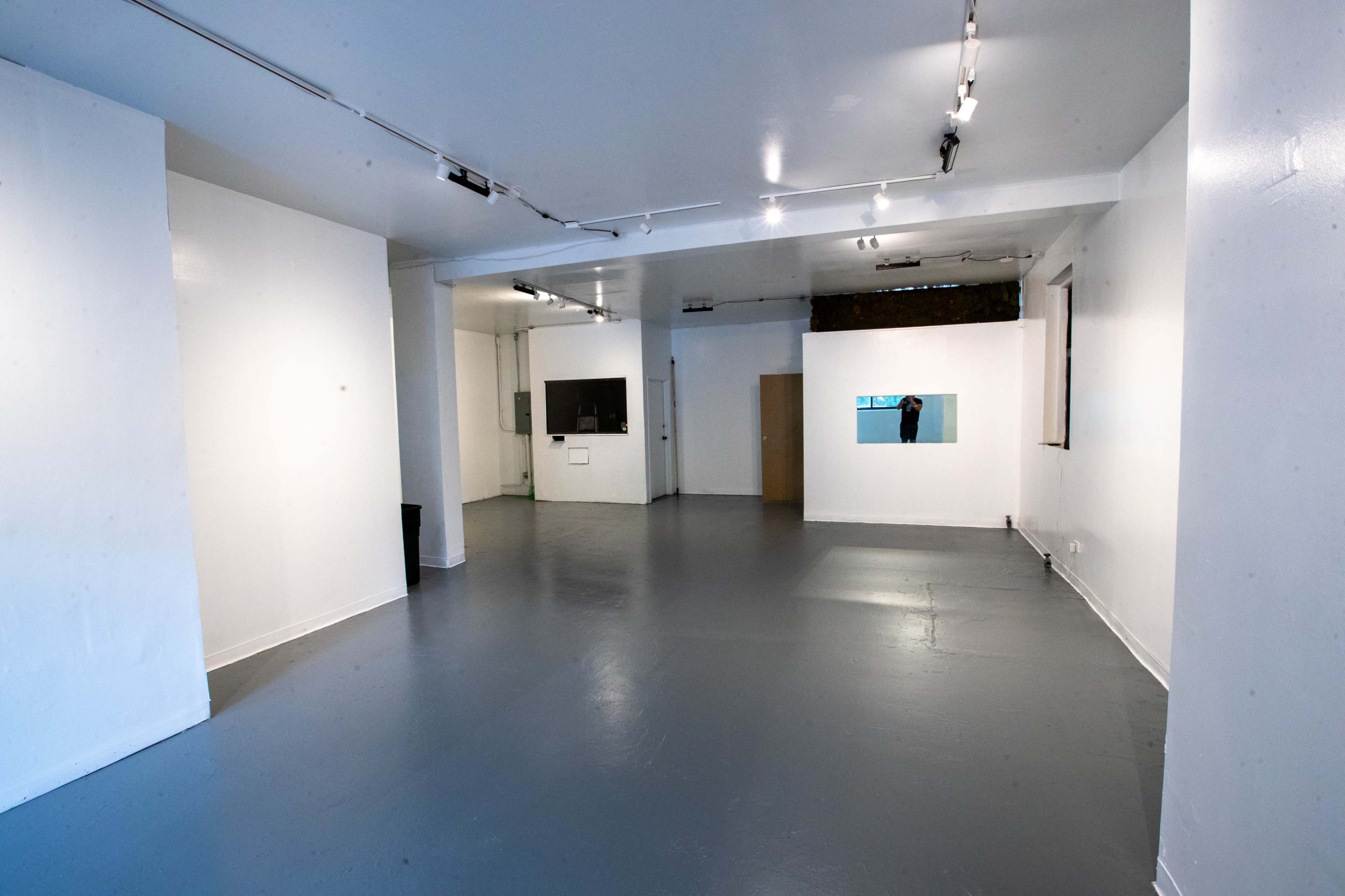 A spacious, empty room with white walls, gray flooring, and a few windows and doors.