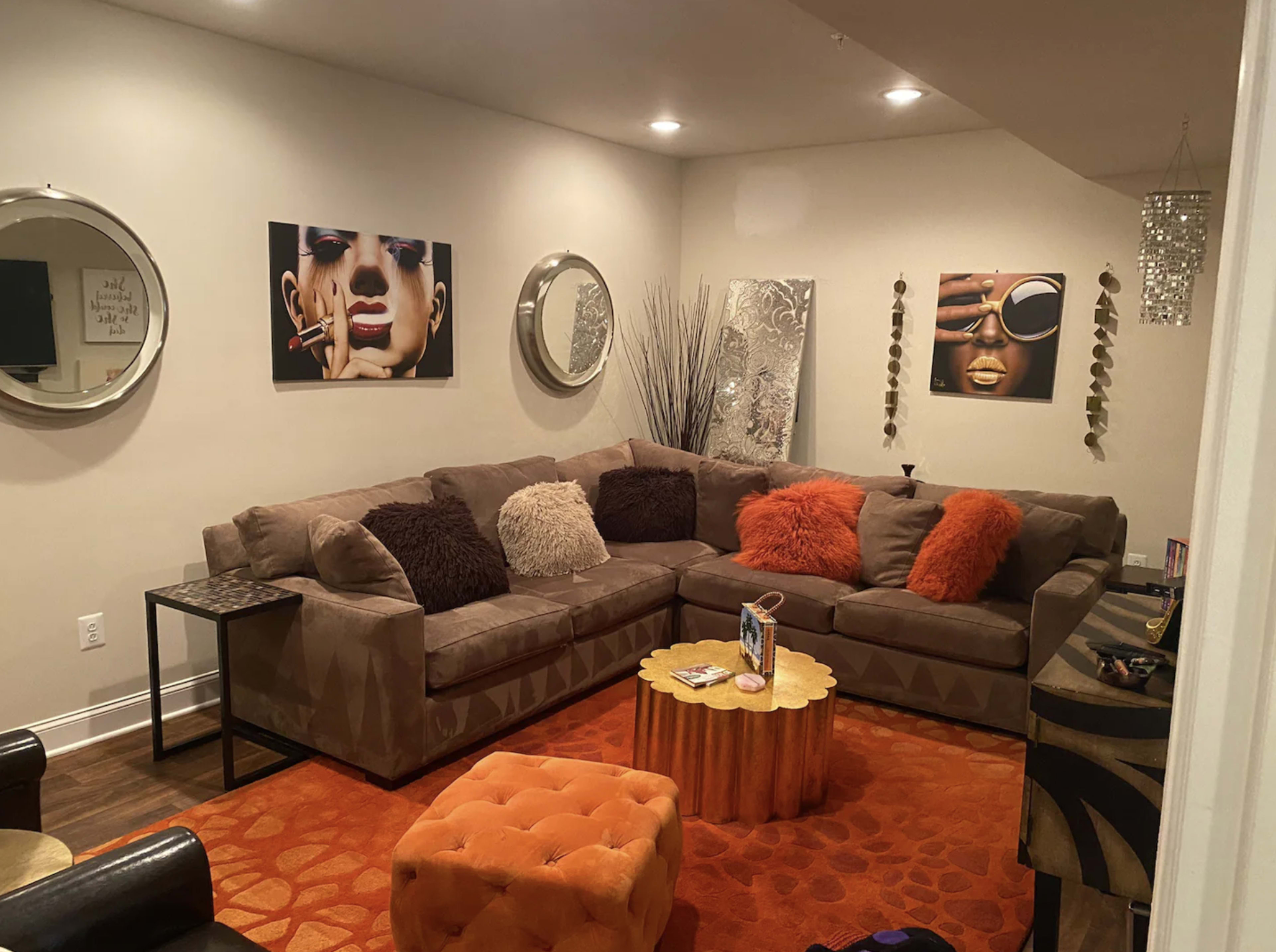A modern living room with a large sectional sofa, orange accents, decorative wall art, and a round coffee table.