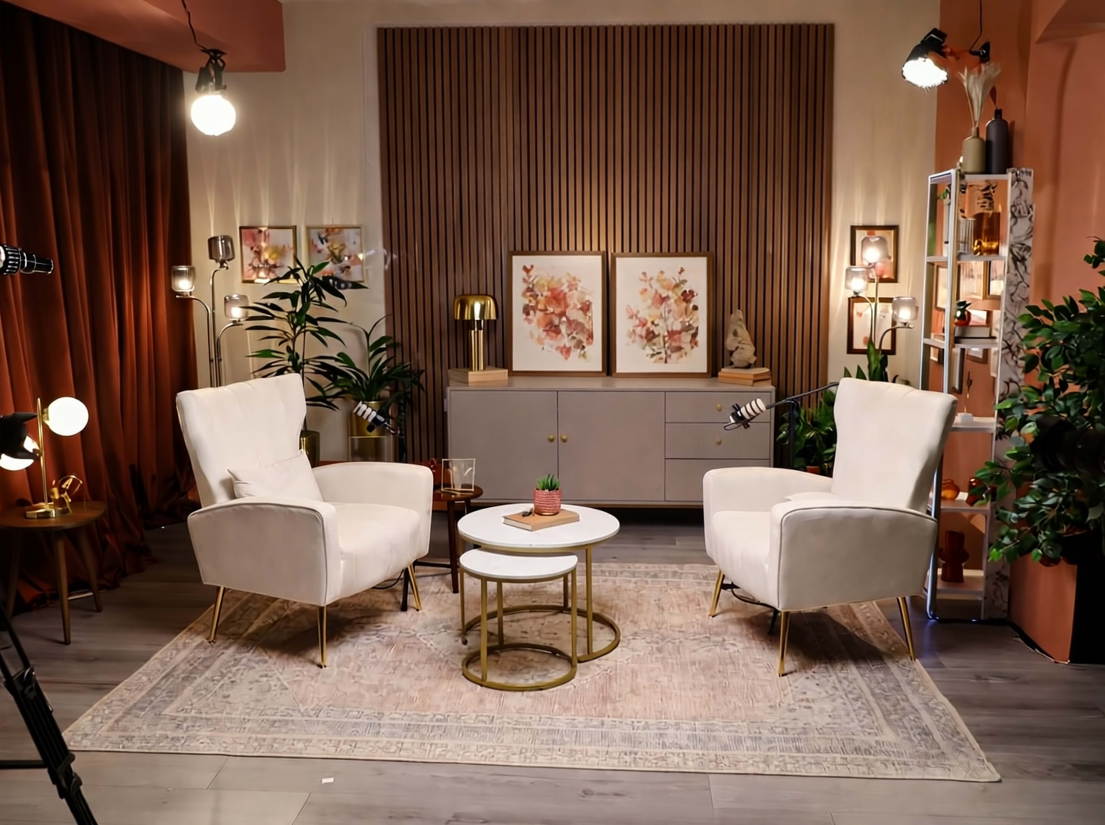 The image shows a modern, cozy sitting area featuring two white armchairs, a round coffee table, and decorative plants, all set against a backdrop of warm colors and tasteful artwork.