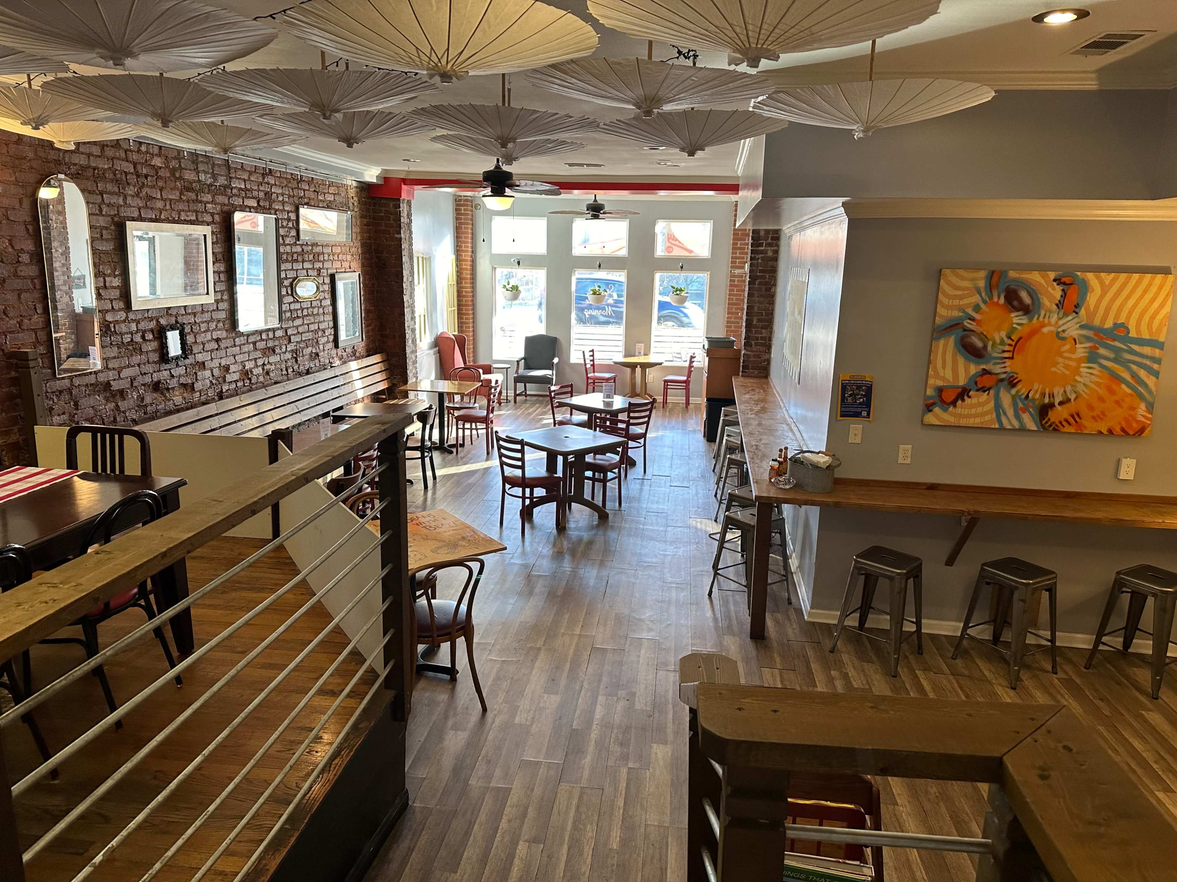 The interior of a restaurant featuring wooden flooring, a mix of tables and chairs, and decorative paper umbrellas hanging from the ceiling.