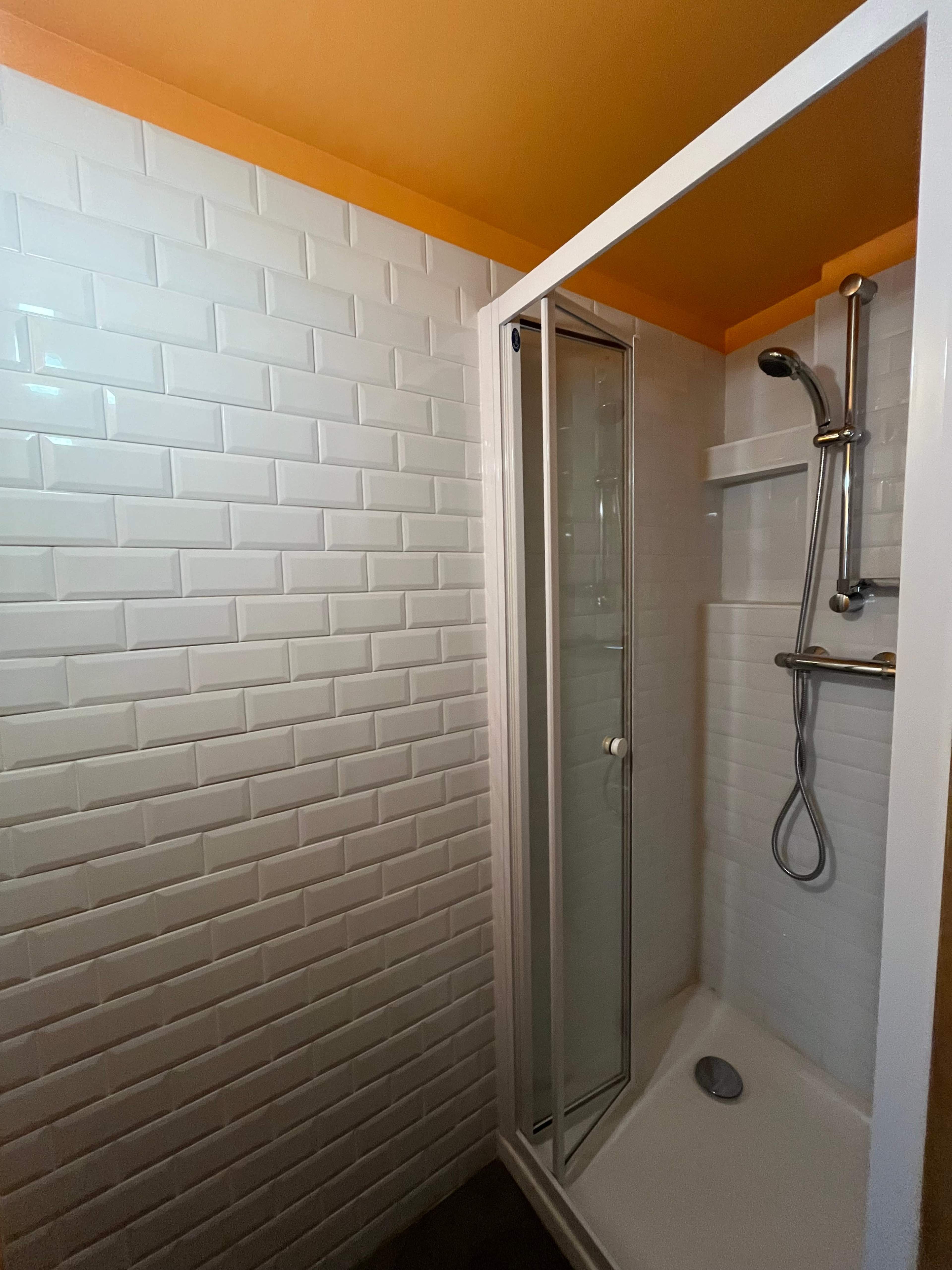 The image shows a modern shower stall with white subway tile walls and an orange ceiling.