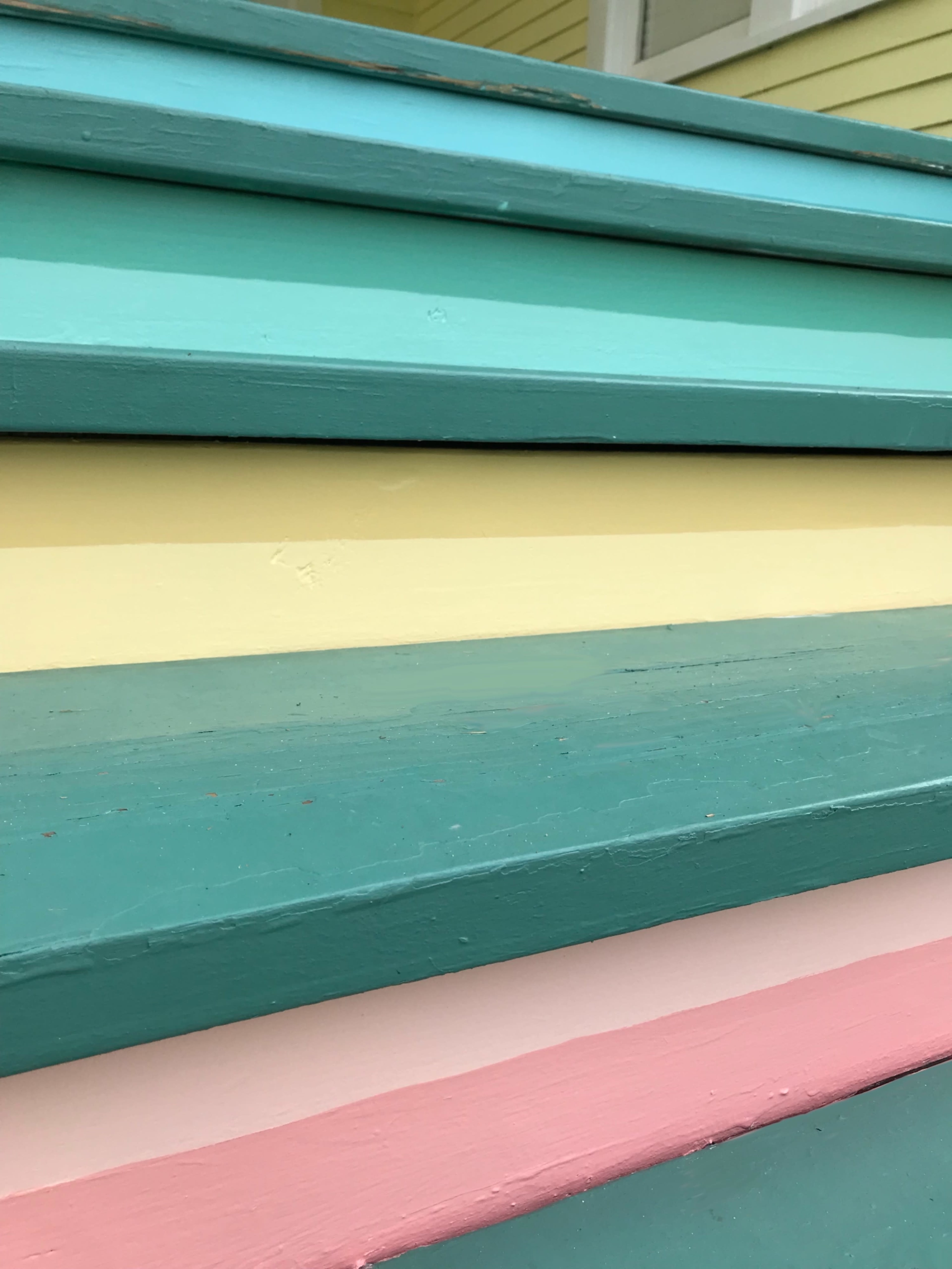 A set of wooden steps painted in horizontal stripes of teal, yellow, and pink.
