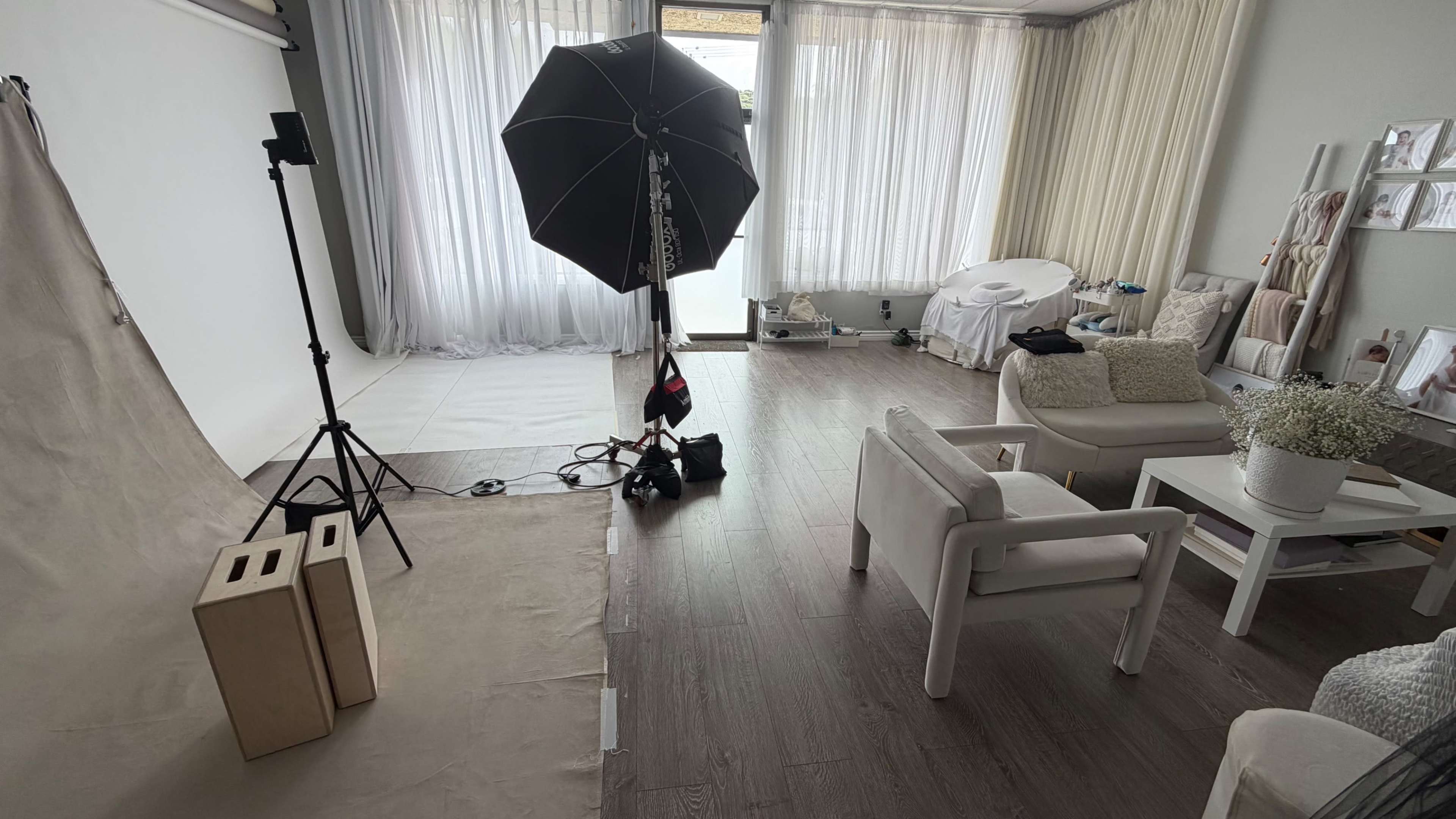 The image shows a photography studio with lighting equipment, a backdrop, and furniture arranged for a photoshoot.