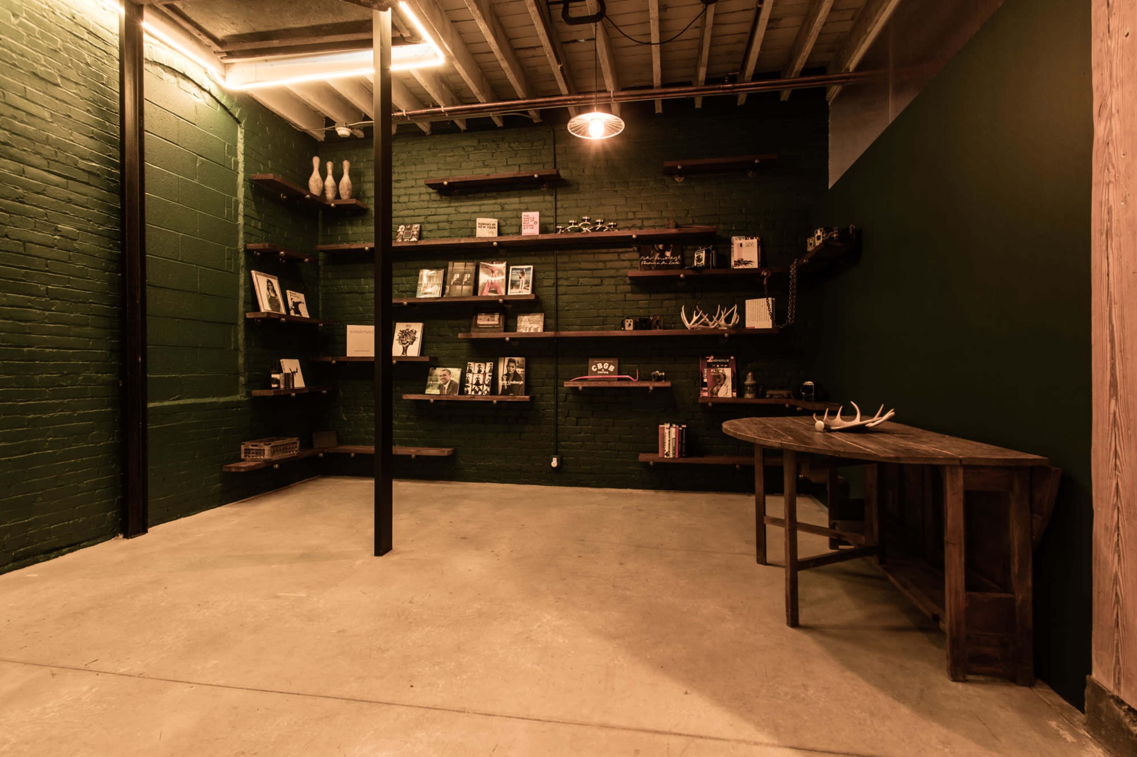 The image shows a room with green brick walls, wooden shelves displaying various items, and a round wooden table positioned against the wall.