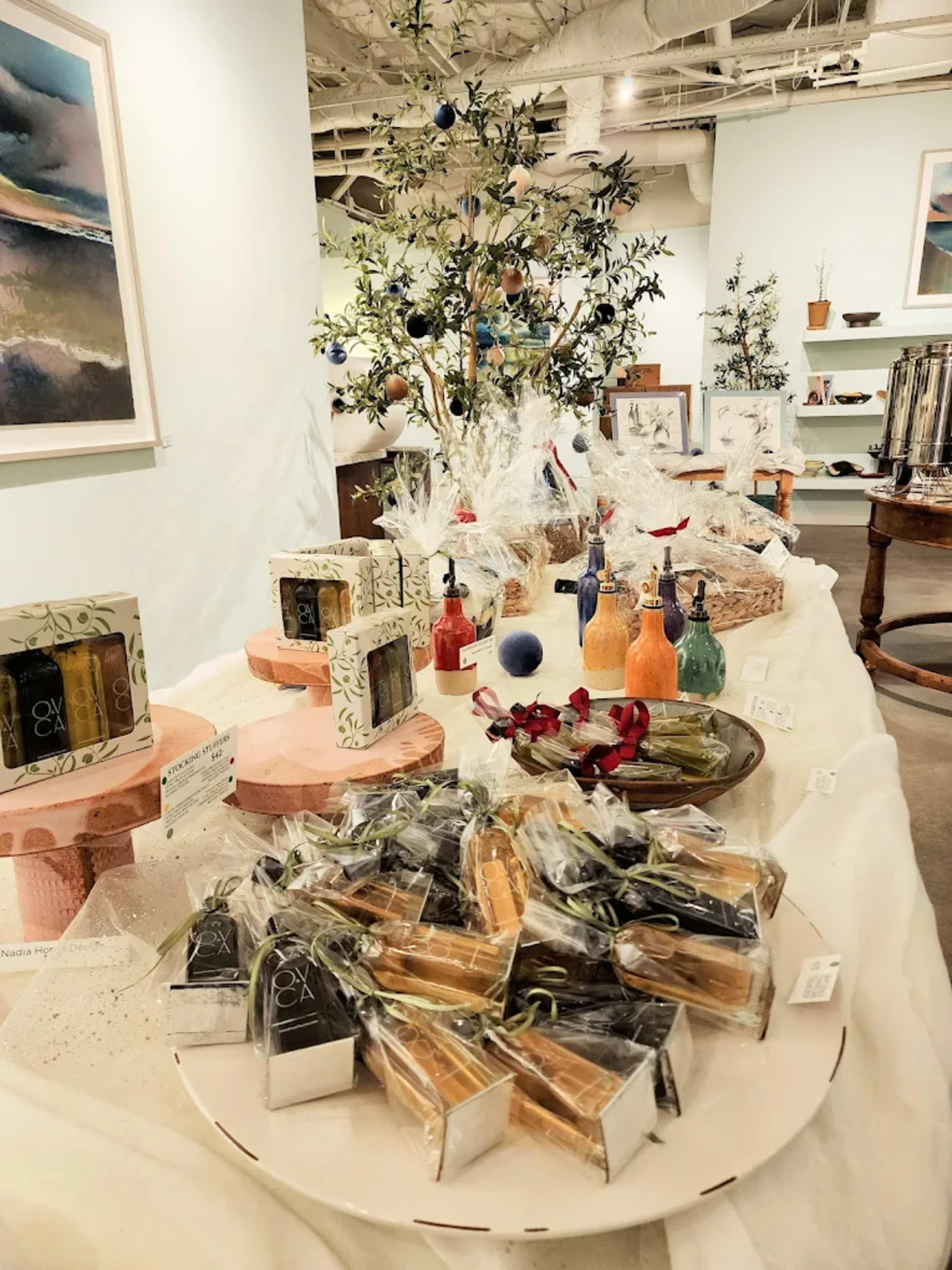 The image shows a well-arranged display of various artisanal products, including soaps and decorative items, on a table in a bright indoor space.