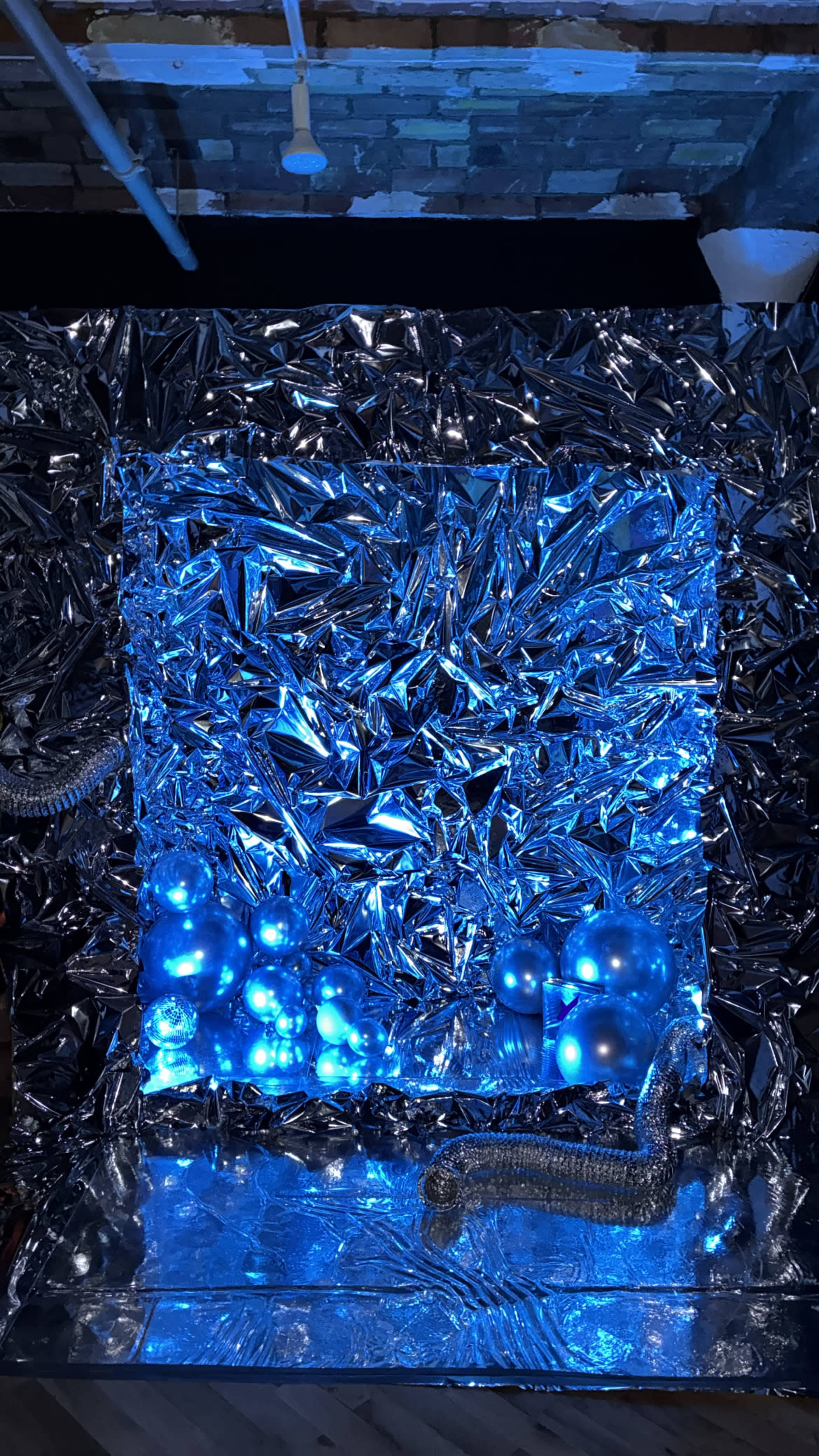 The scene features a backdrop made of crumpled silver foil illuminated by blue lighting, with several blue spheres and a metallic structure in the foreground.
