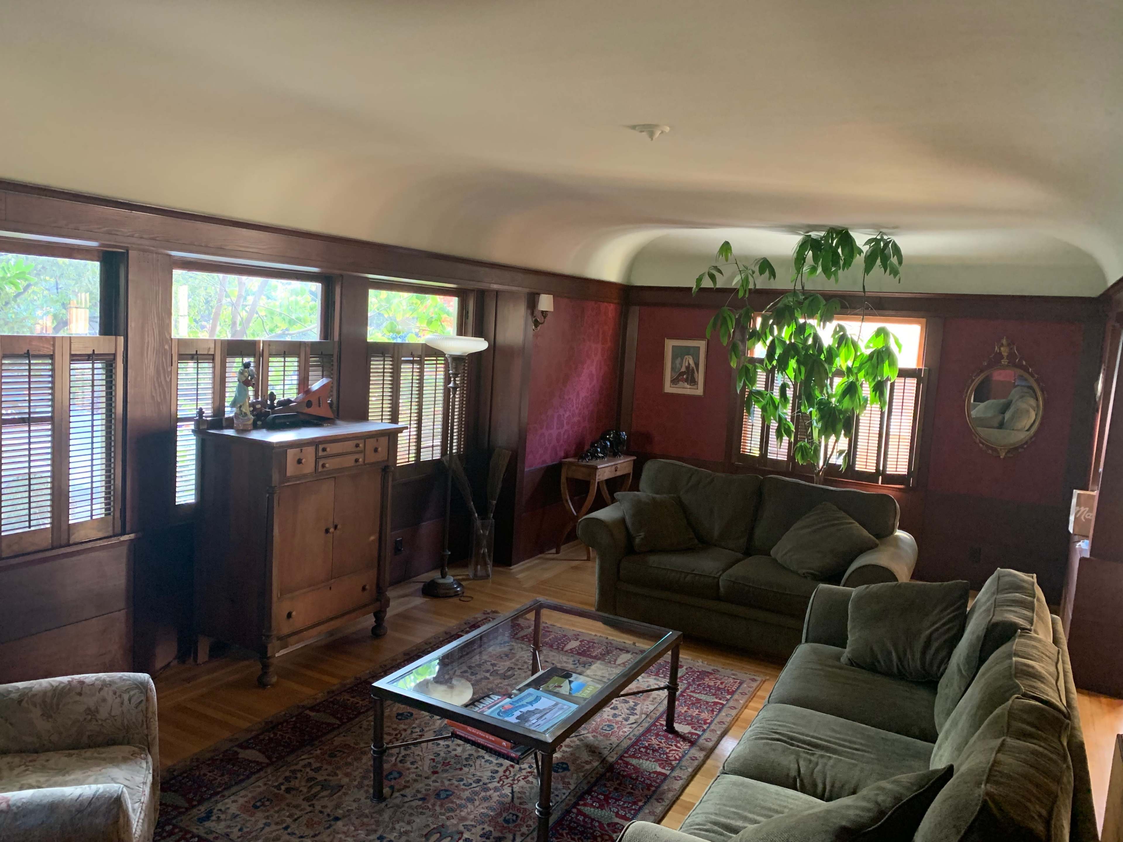 The room features a seating area with a green sofa and armchair, a wooden cabinet, and large windows allowing natural light to enter.