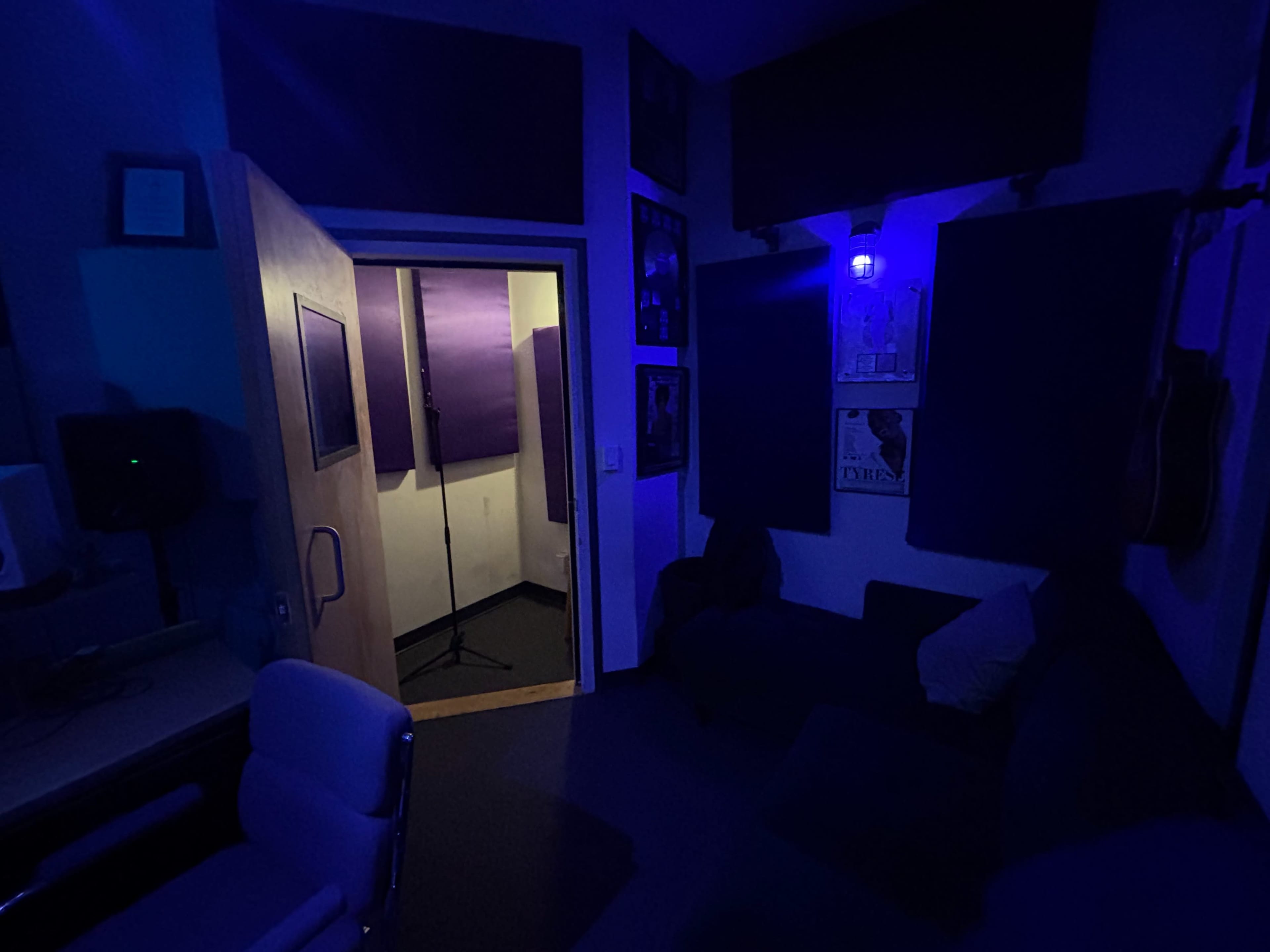 The image shows a dimly lit recording studio with a soundproof booth visible through an open doorway.