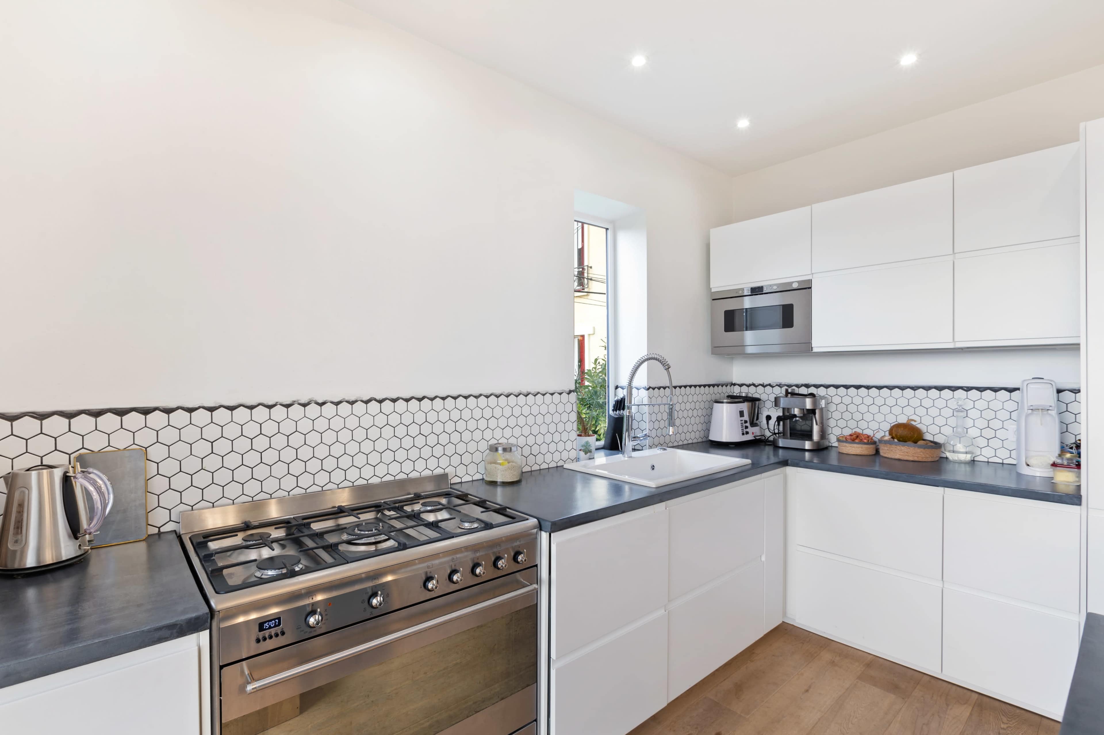 A modern kitchen features a gas stove, a sink, and built-in appliances with white cabinetry and hexagonal tile backsplash.