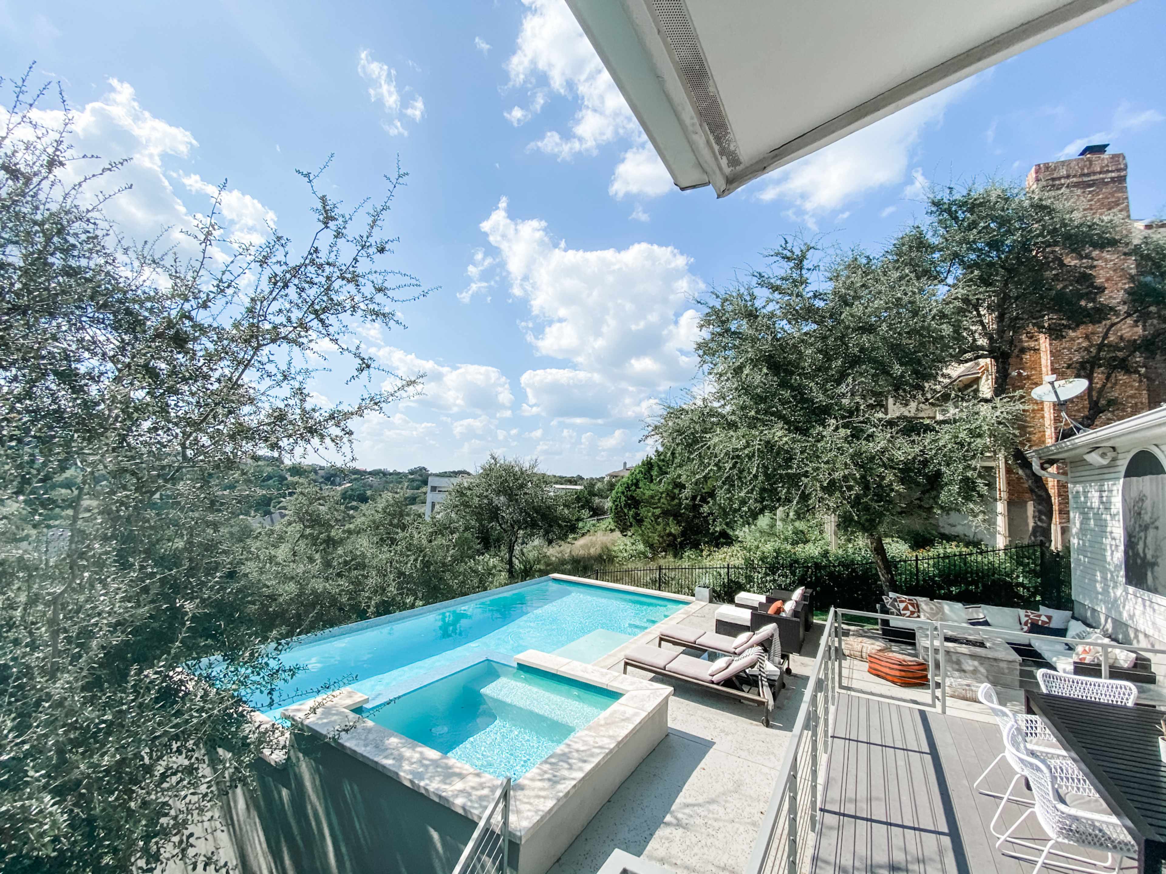 A modern outdoor pool surrounded by lounge chairs and greenery under a partly cloudy sky.