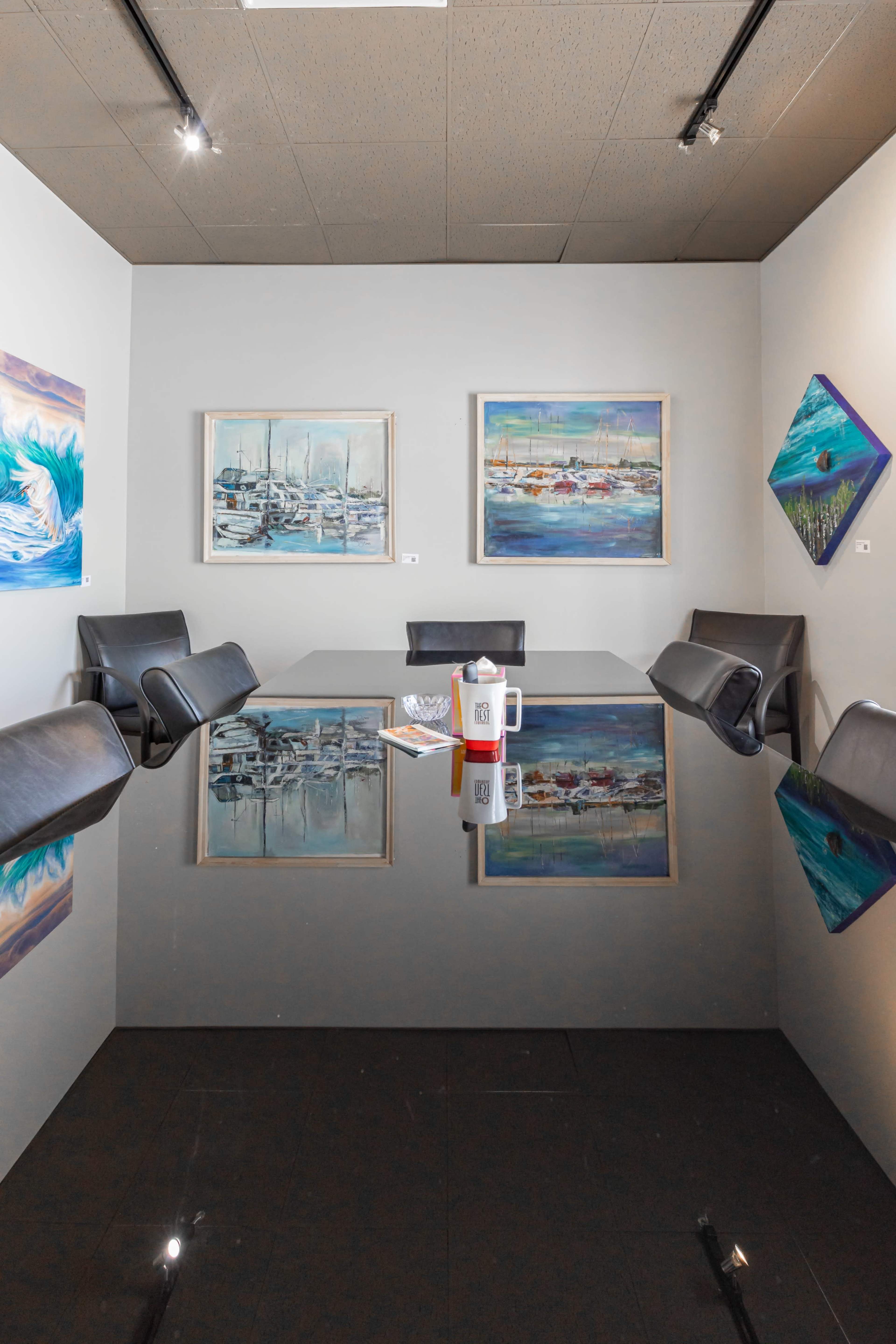 A modern conference room features a reflective black table surrounded by leather chairs and adorned with colorful maritime-themed artwork on the walls.