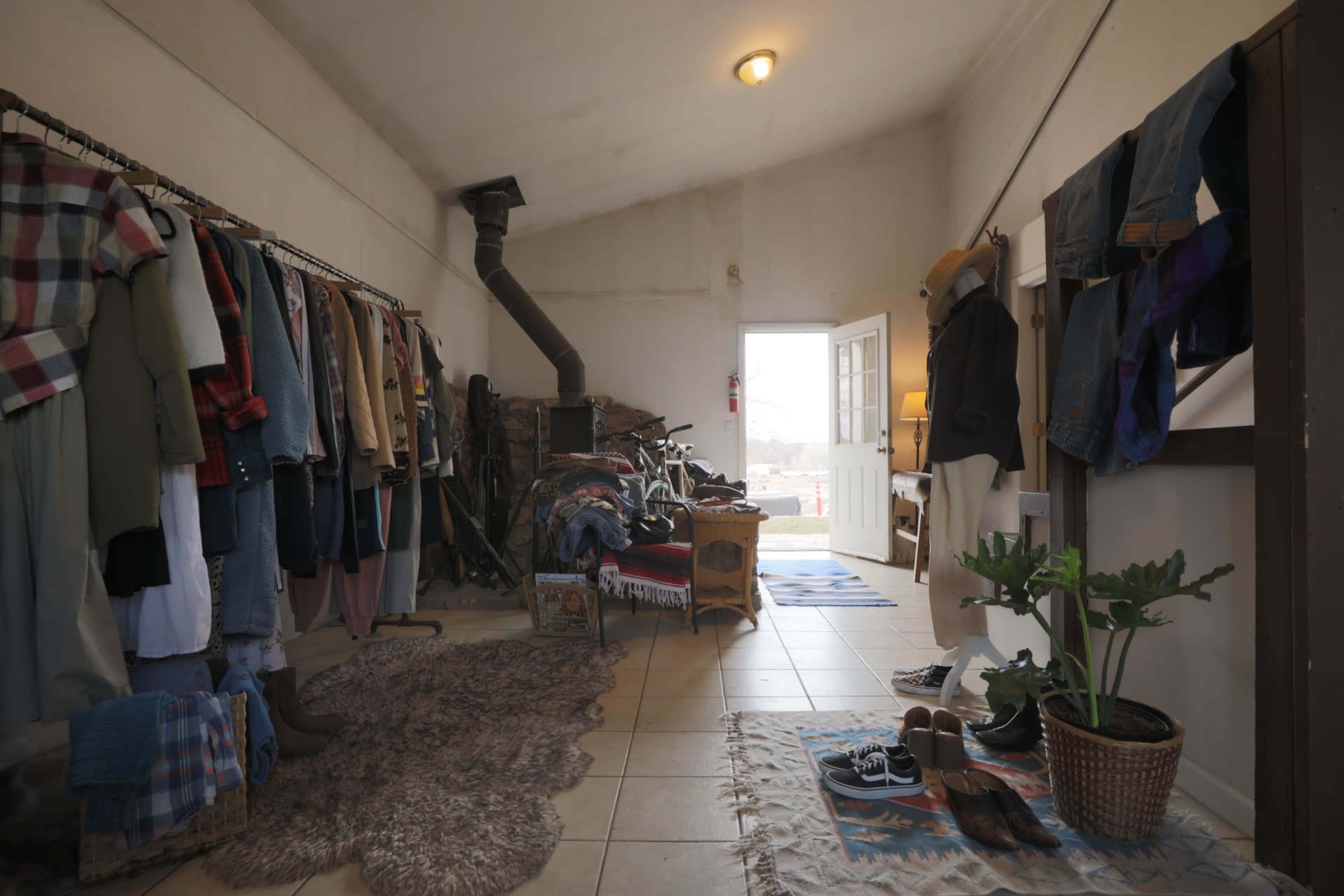 The image shows an interior of a clothing store with racks of garments on one side and an entrance leading outside on the other.
