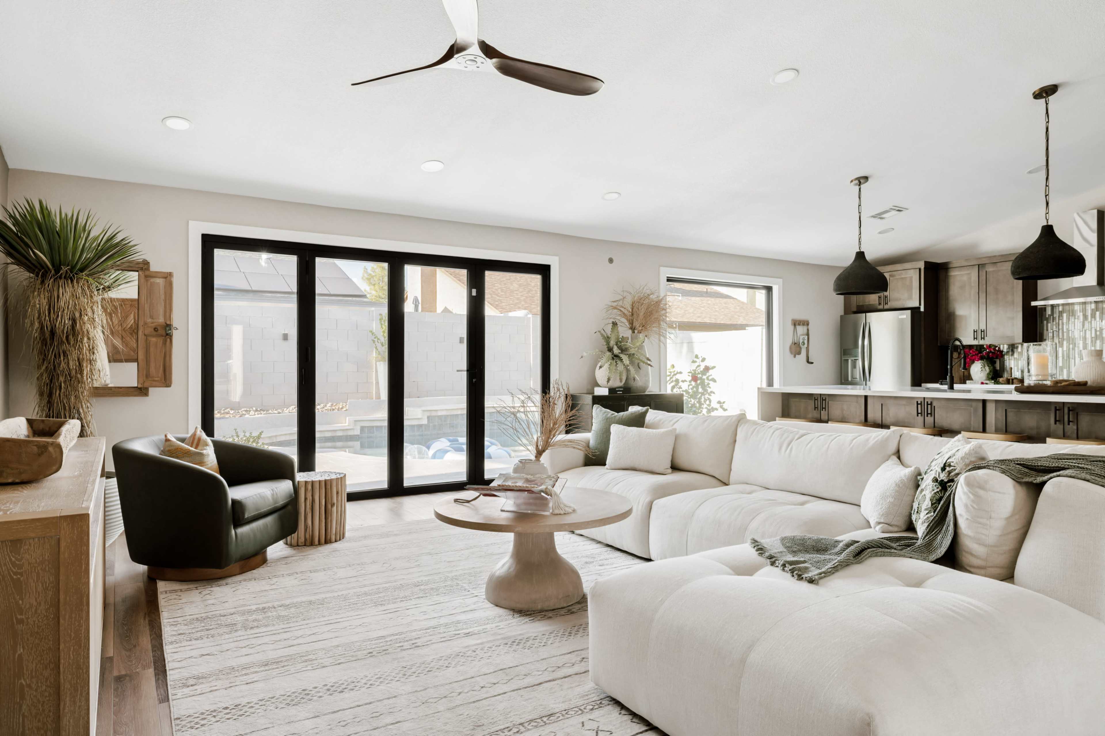 The living room features a large sectional sofa, a round coffee table, and large glass doors that open to a backyard pool area.