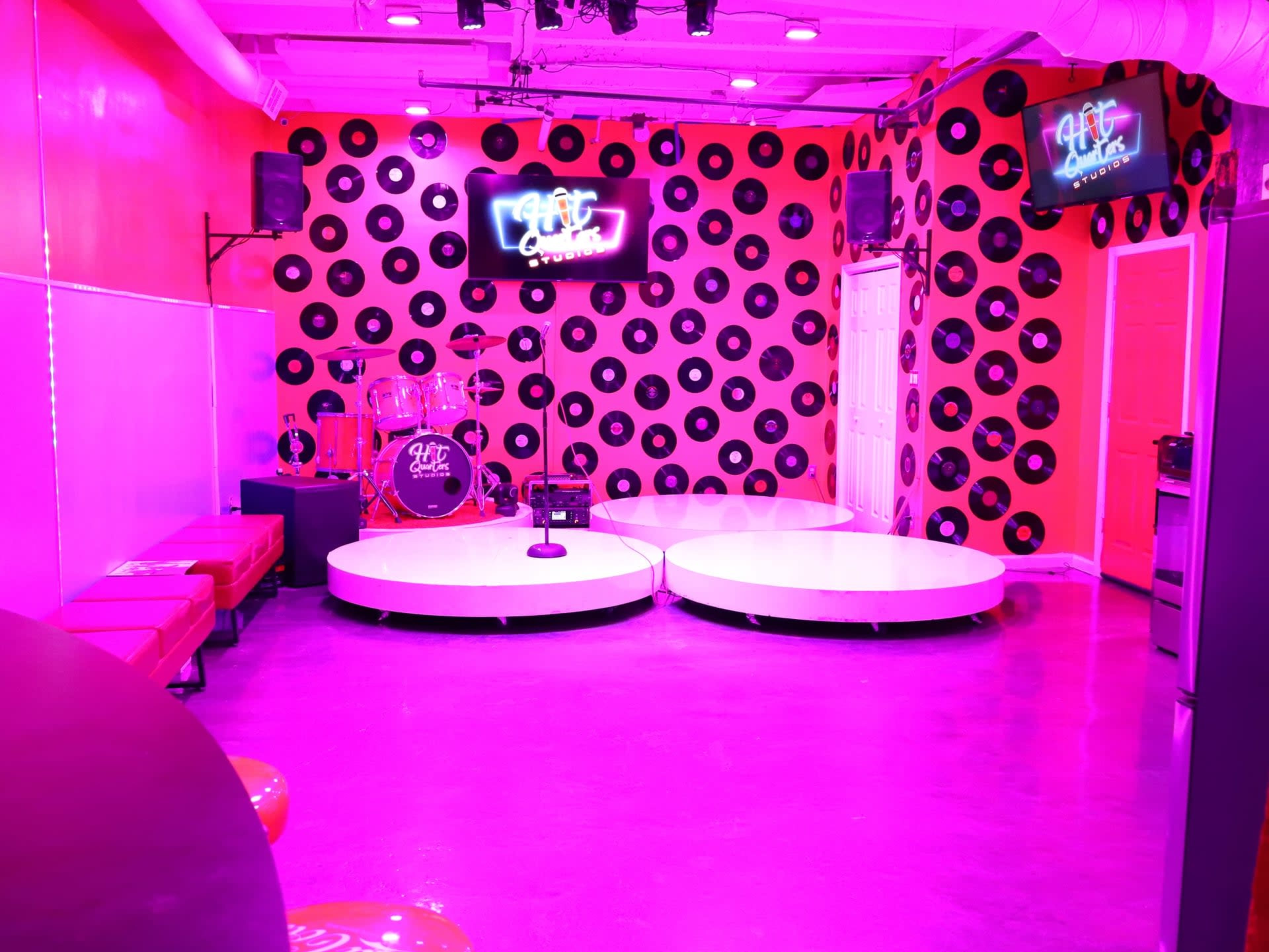 The image shows a vibrant music venue with a circular stage, decorated with a pink and black polka dot wall and neon signs.