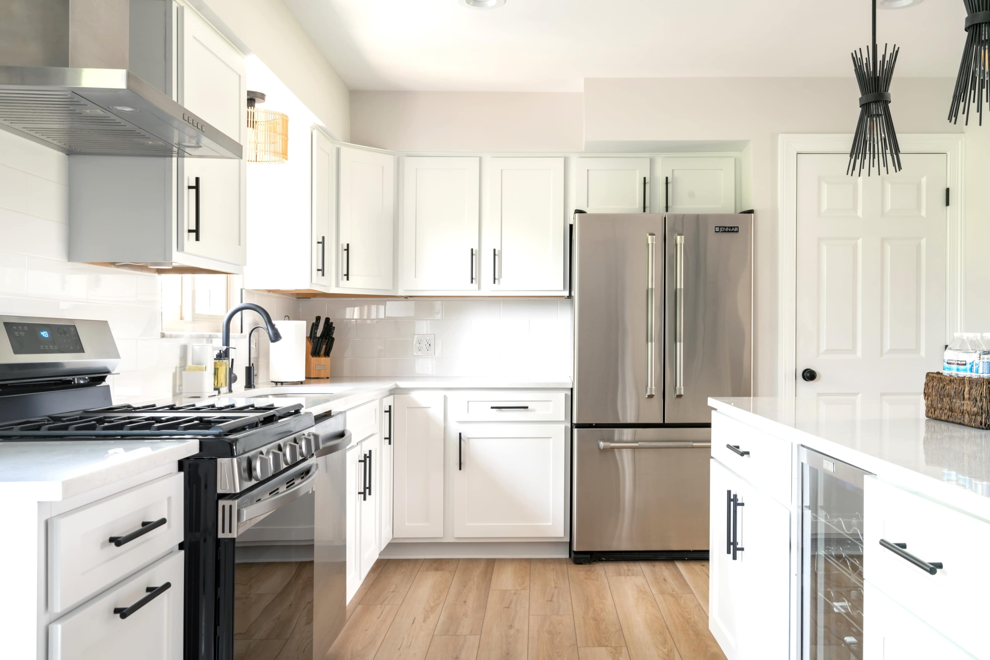 A modern kitchen with white cabinetry, stainless steel appliances, and a light wood floor.