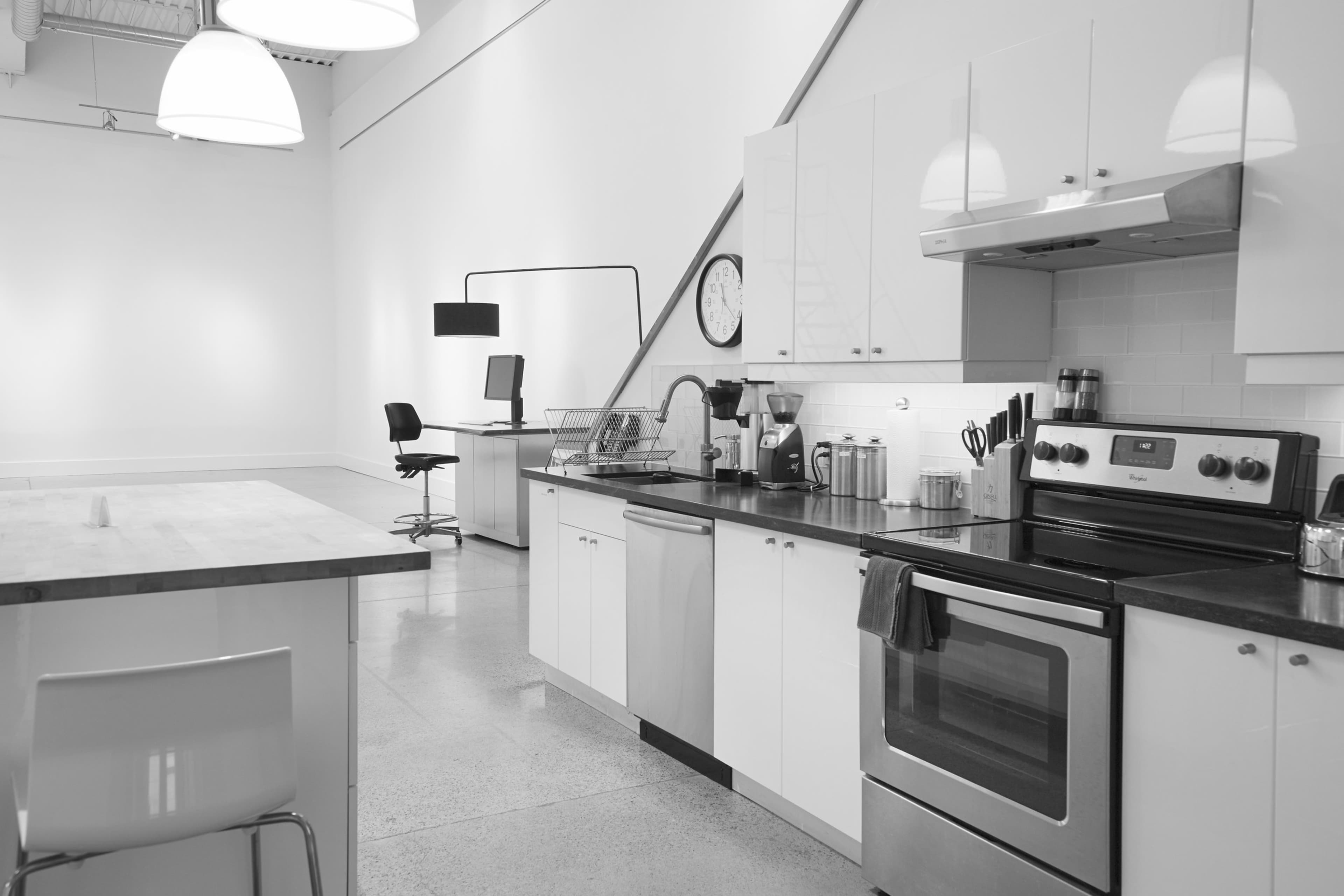 A modern kitchen with white cabinets, a stainless steel stove, and a minimalist workspace in the background.