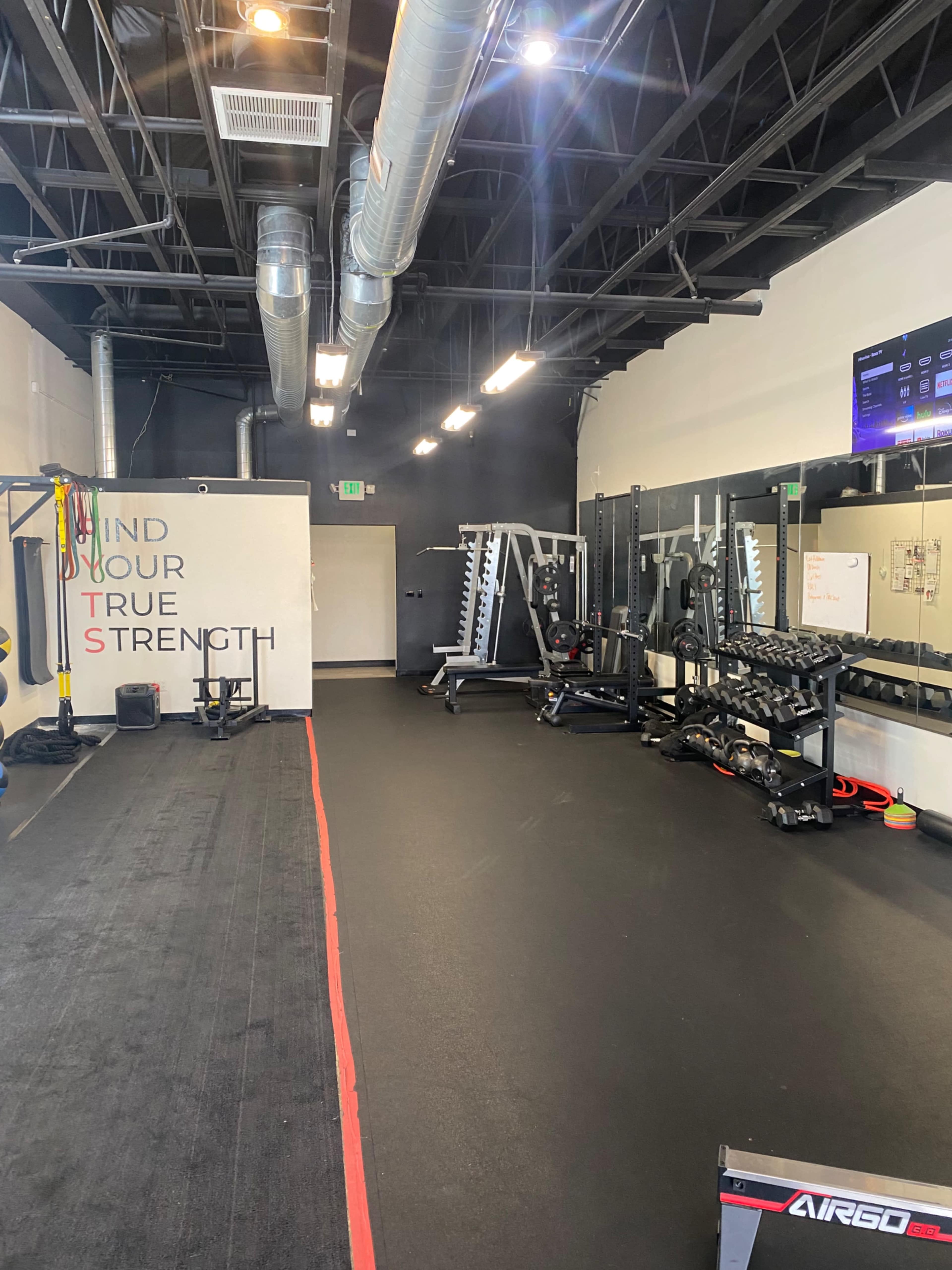 A fitness gym with various exercise equipment, including weights and resistance bands, along with a motivational wall and mirrors.