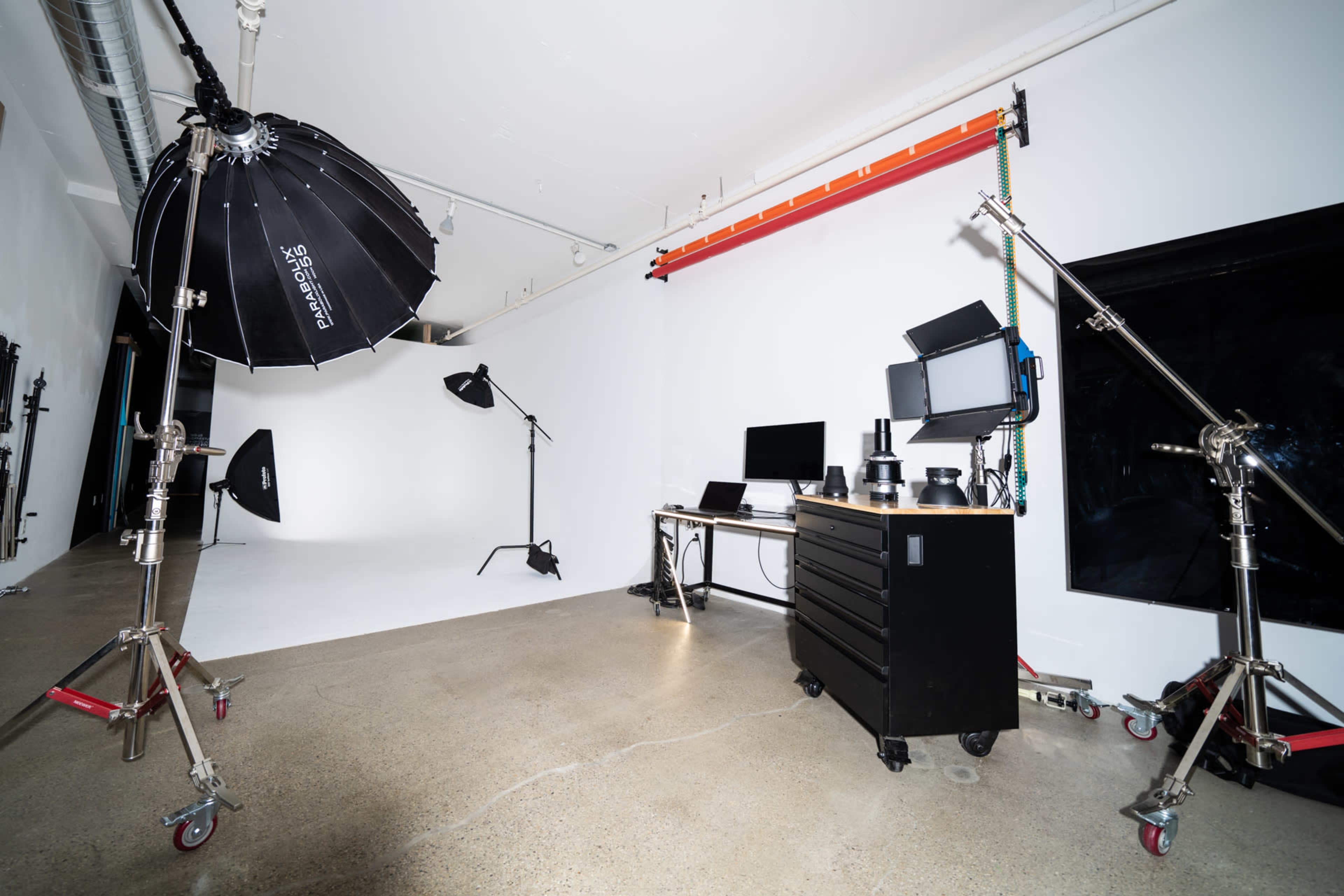 A photography studio with various lighting equipment, a computer setup, and a plain white backdrop.
