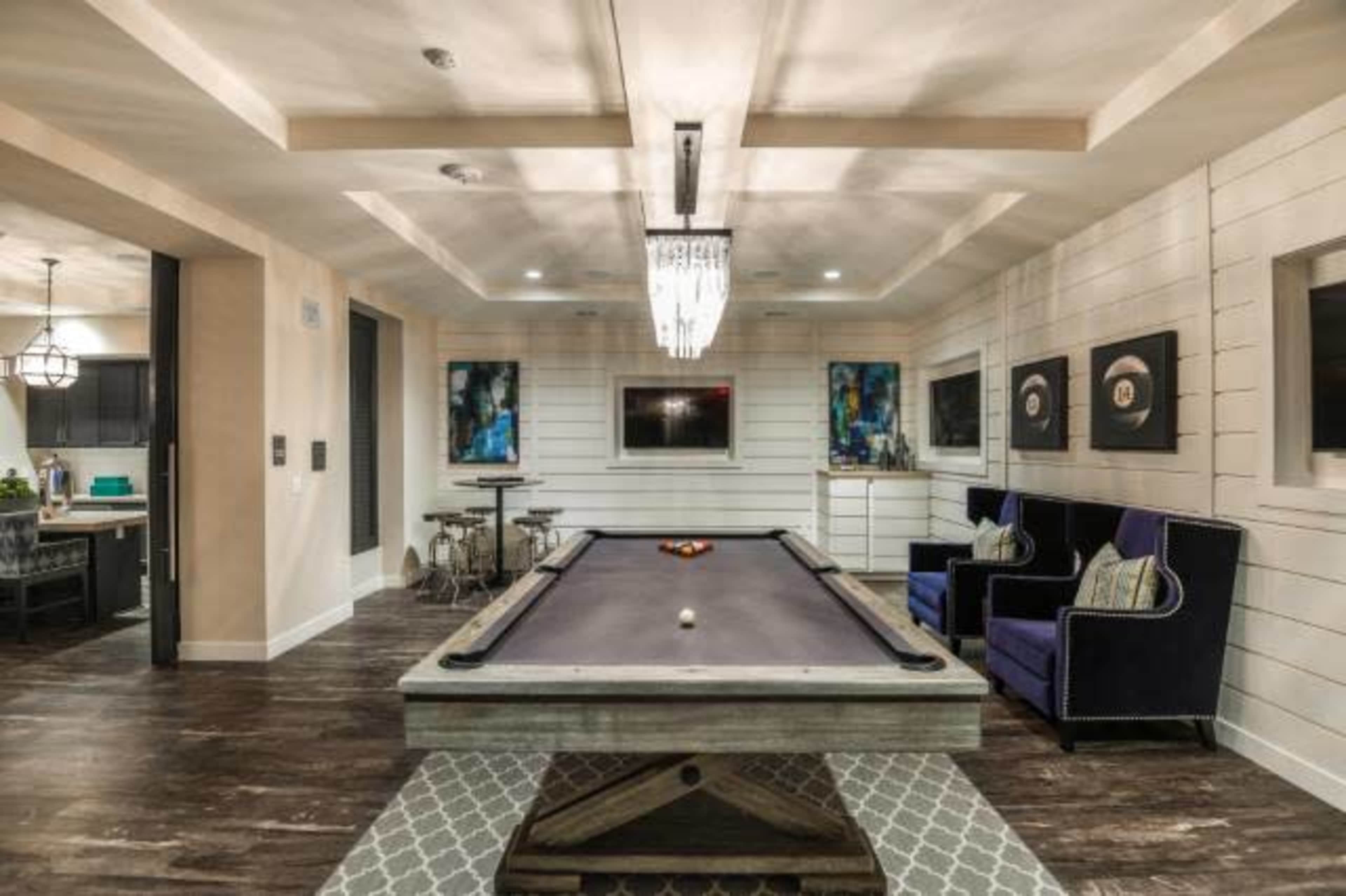 A recreational room with a billiard table, surrounded by plush seating and modern decor.