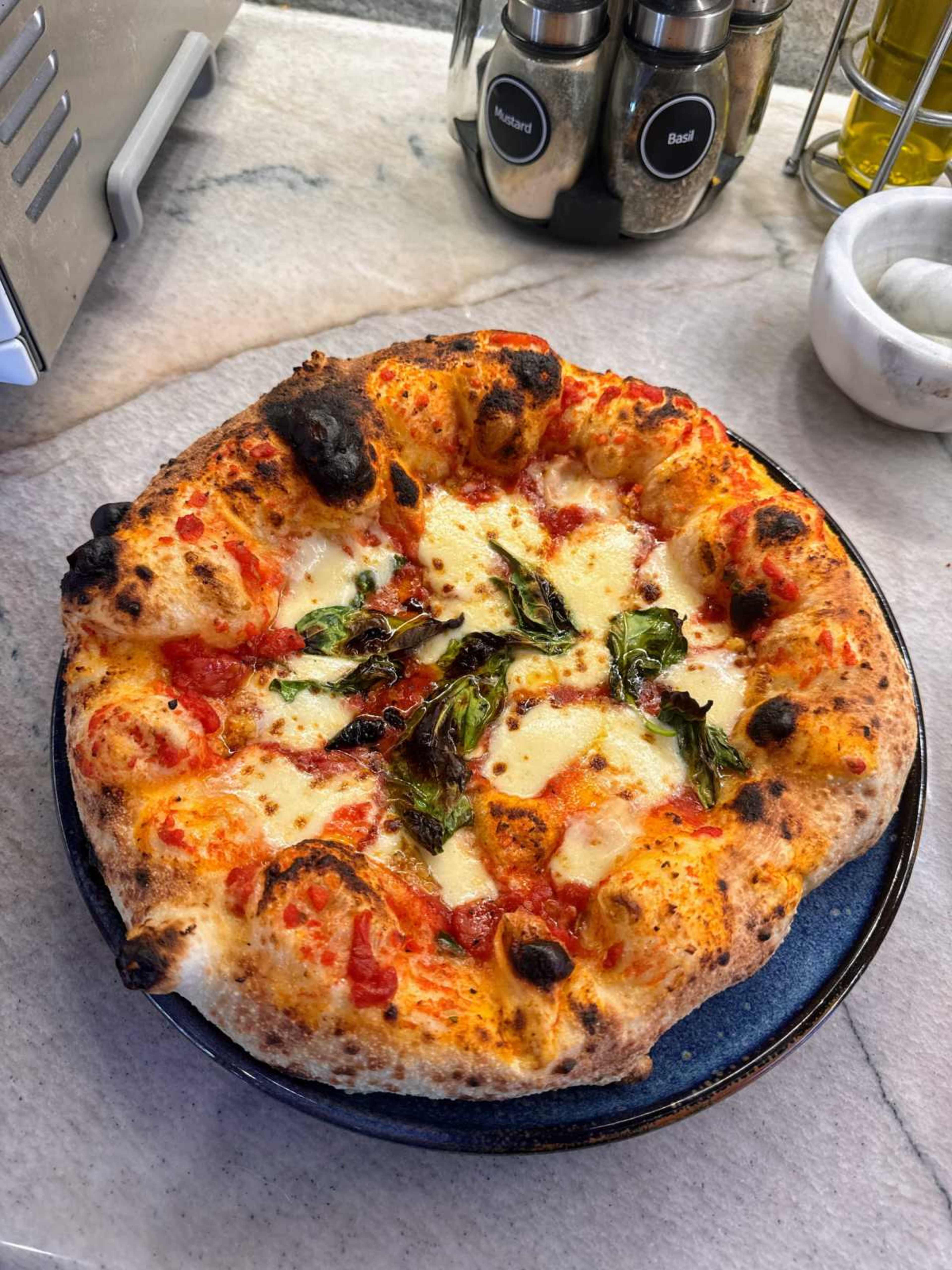 A freshly baked pizza garnished with melted cheese and basil sits on a blue plate.